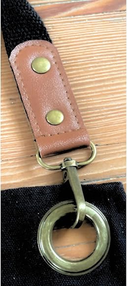 A metal clasp attached to a brown leather strap with brass rivets, linking to a brass ring on a black fabric.
