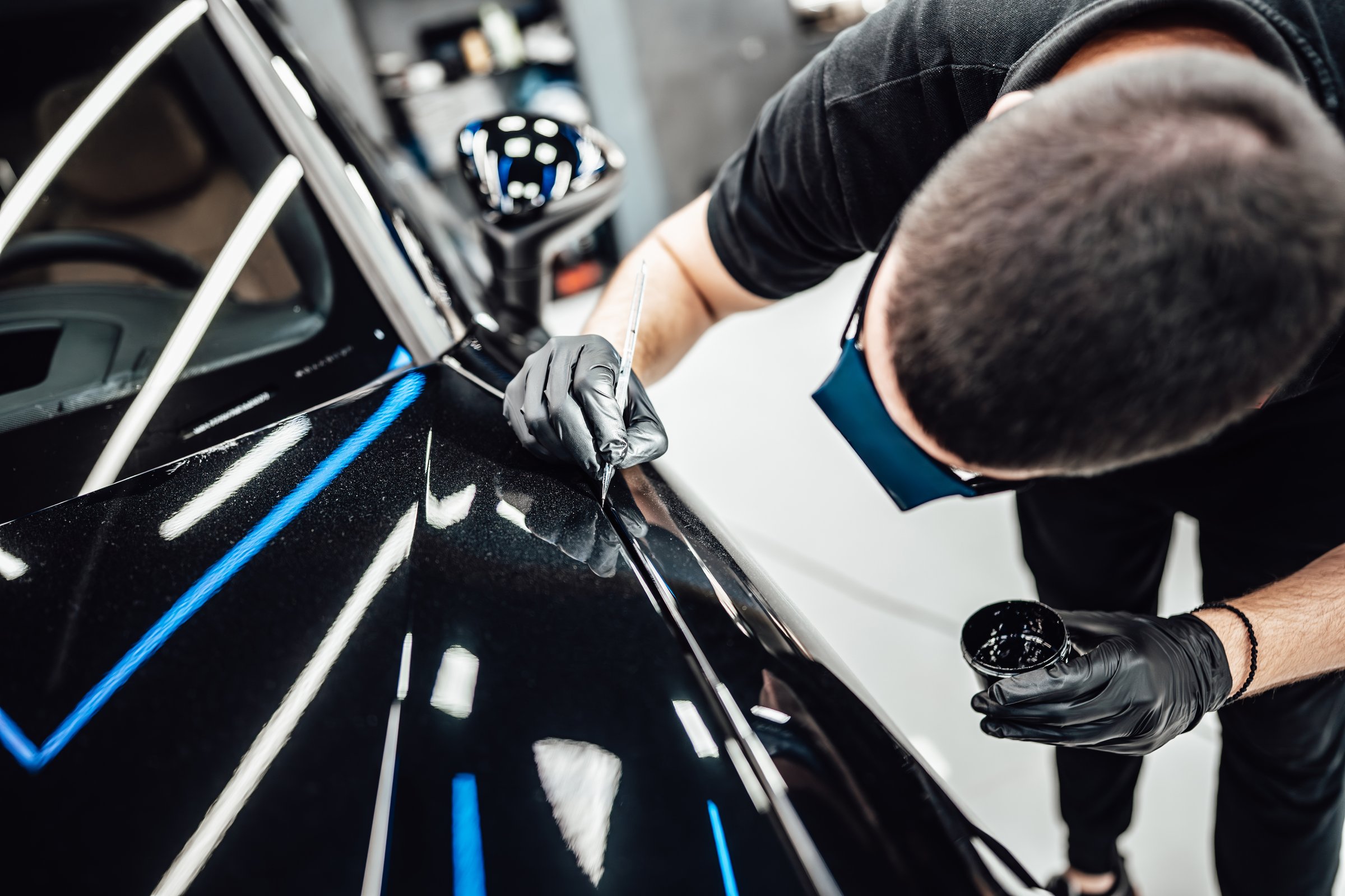 Professional worker fixing luxury car scratches at car detailing and valeting service center. Selective focus.