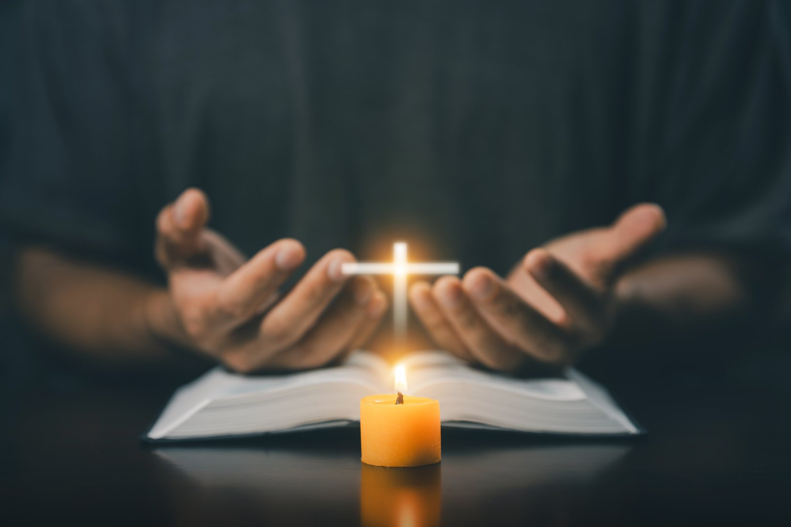 Christian man worship. Hands folded in prayer on a Holy Bible in home concept for faith. Spirituality and religion. Man praying on holy bible with candle light. Man hand with Bible praying.