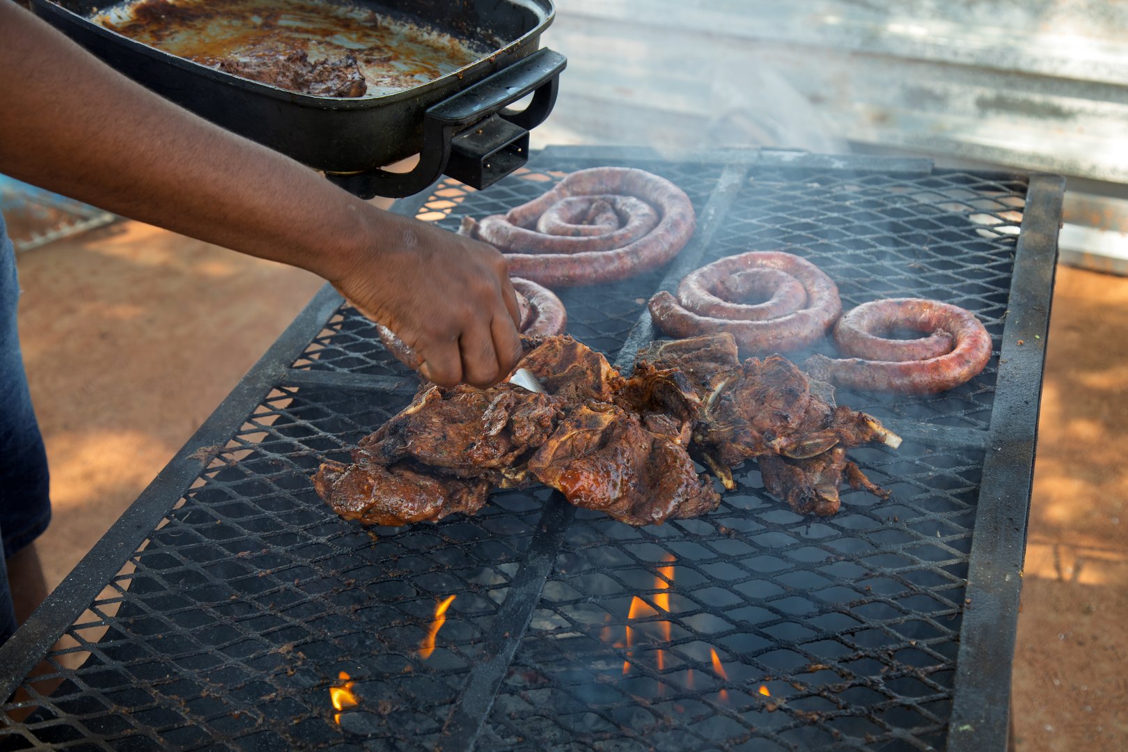 cooking barbeque, african american man turning the meat and the sausages with a fork, american traditional favorite and south african Braai
