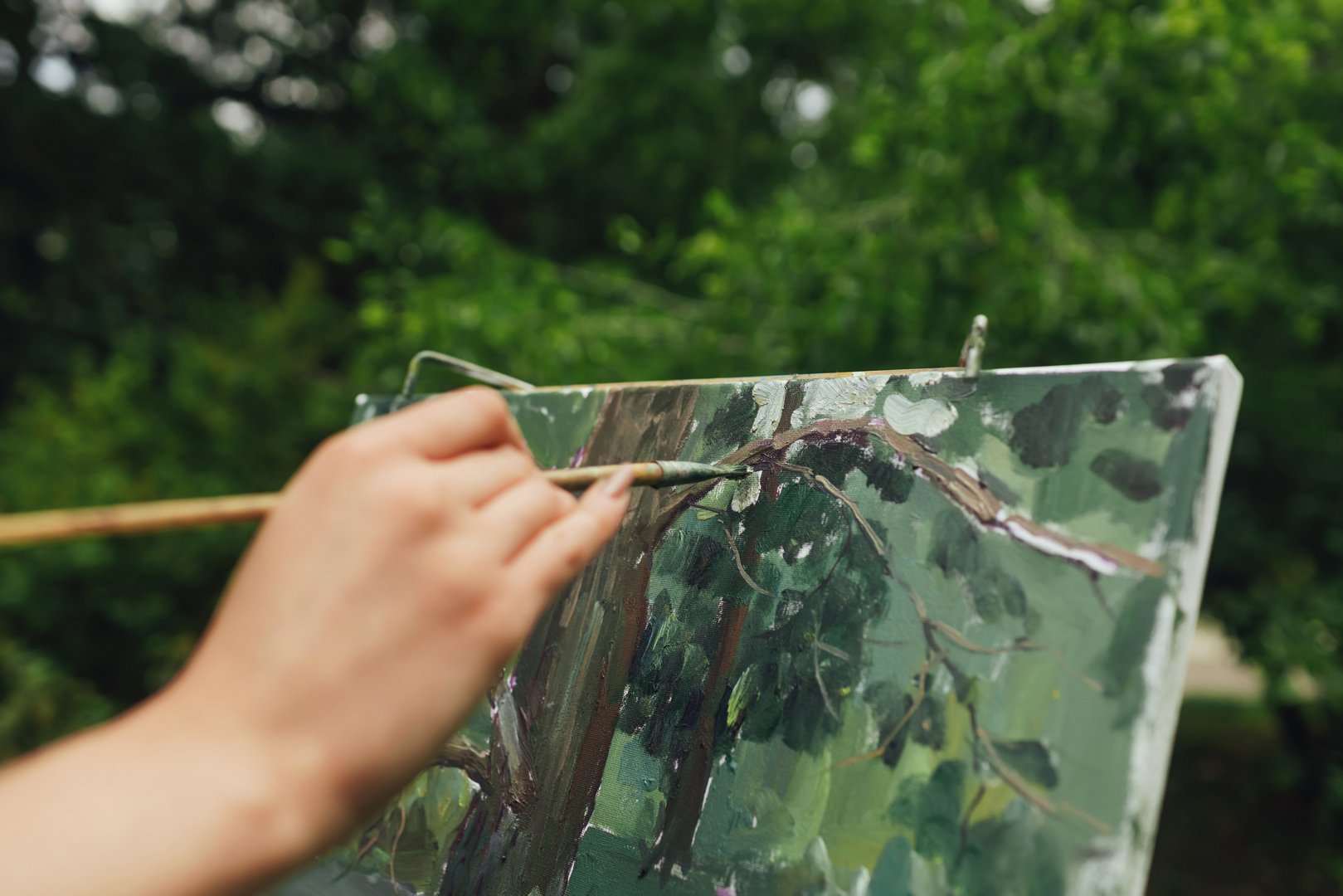 Close up of woman's hands with brushes and paints near a canvas with etude. Mindfulness, art therapy, creativity concept. Process of plein air painting in nature. A series of photos showing the step-by-step creation of a painting