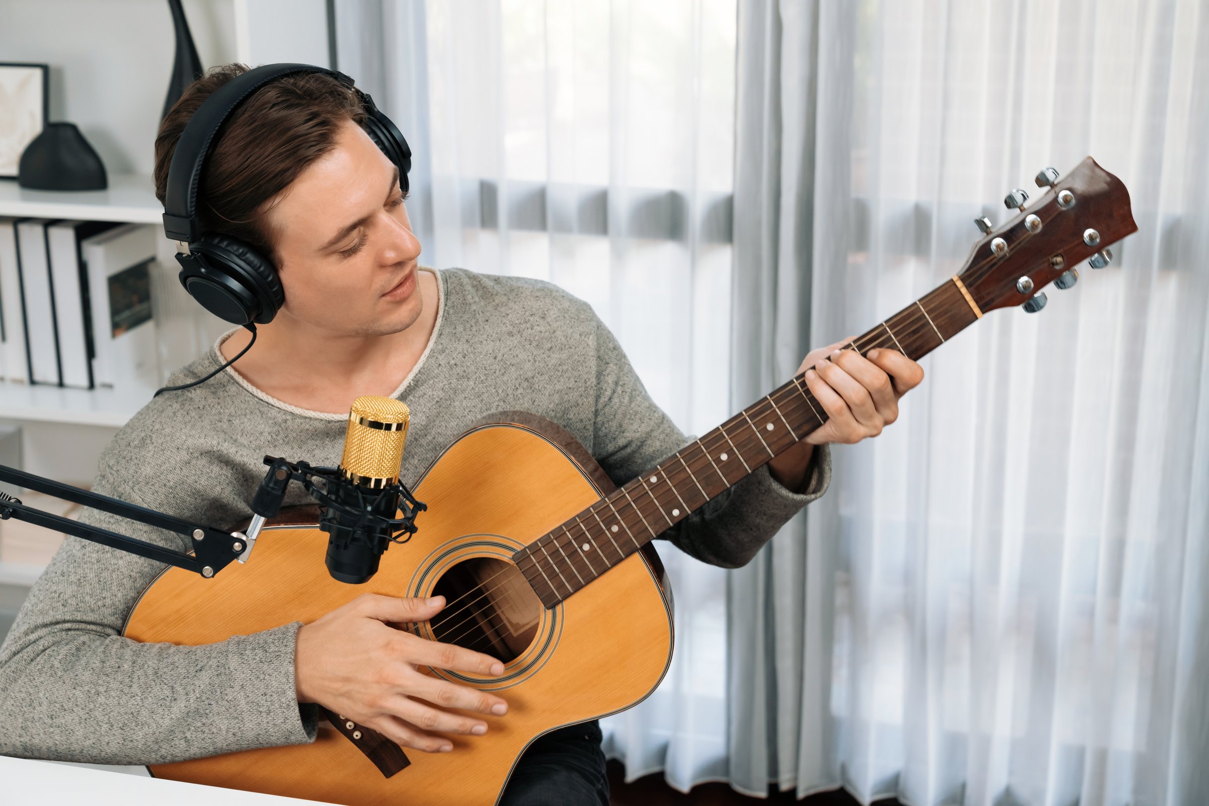 Host channel in smart singer with smiling face, playing guitar along singing, broadcasting on social media channel, wearing headphones to record video streamer at modern studio recording. Pecuniary.