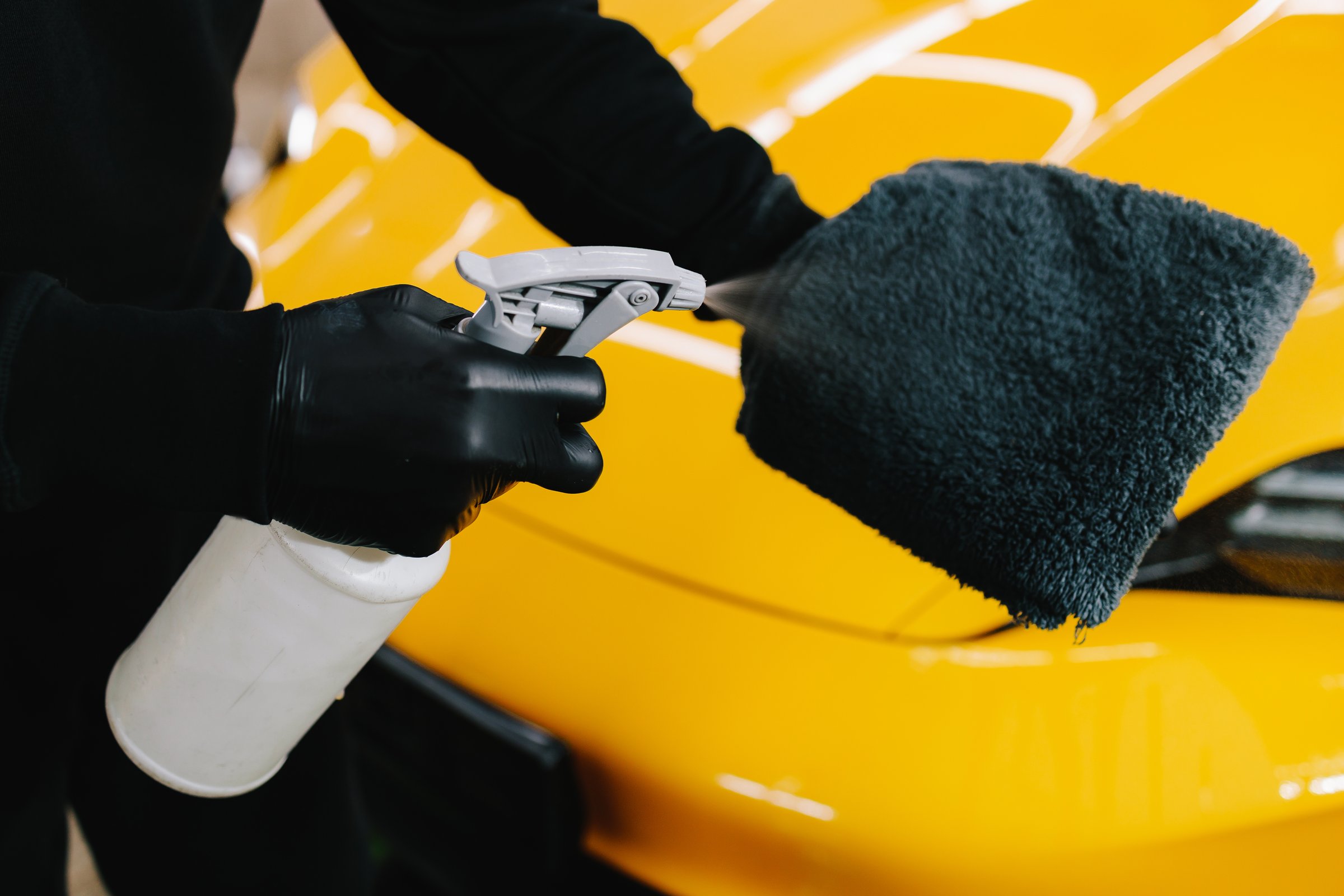 Car cleaner spraying liquid for waxing on microfiber cloth at the service. Detailing process with using spray wax product for car protection