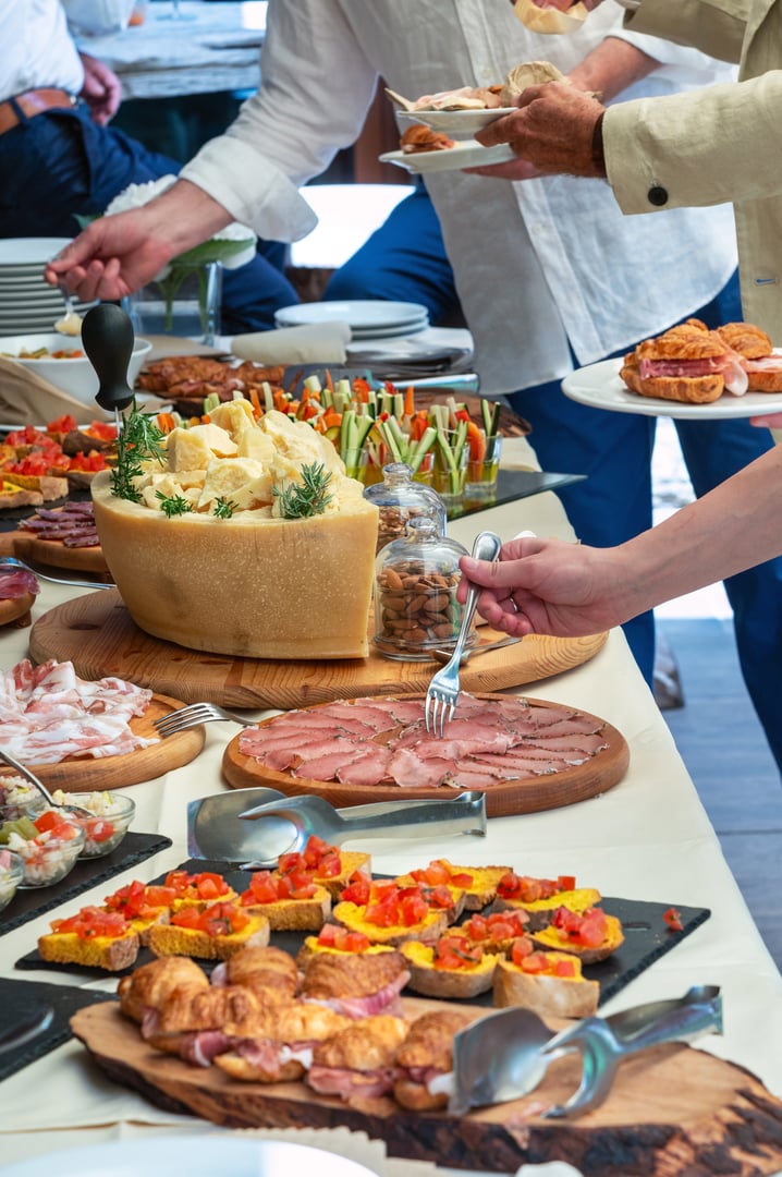 People are serving themselves from a table full of italian cured meat, cheese and other delicious food during a catered event