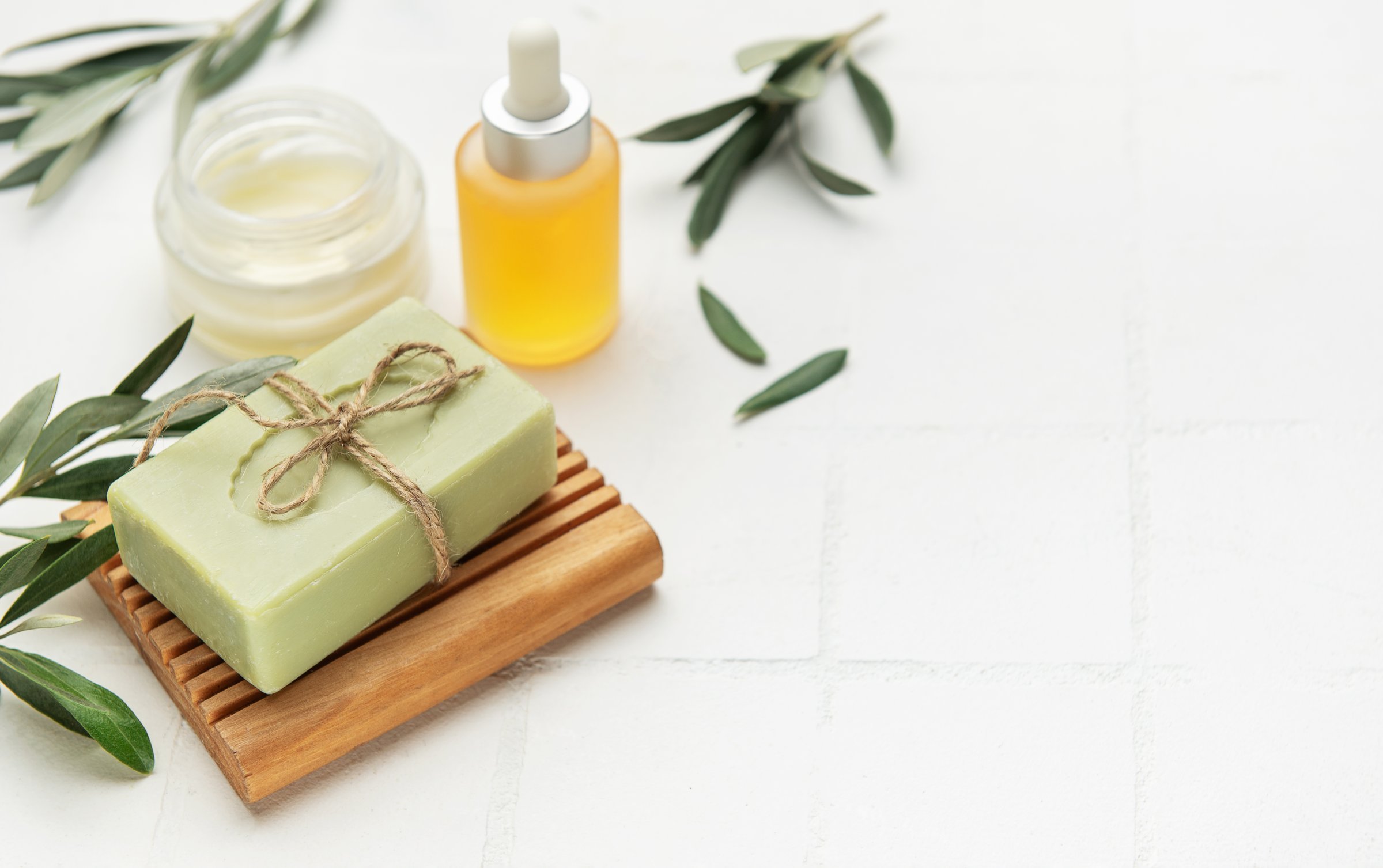 Handmade olive soap, essential oil and cream with olive tree leaves on white background promoting natural skincare and spa treatments