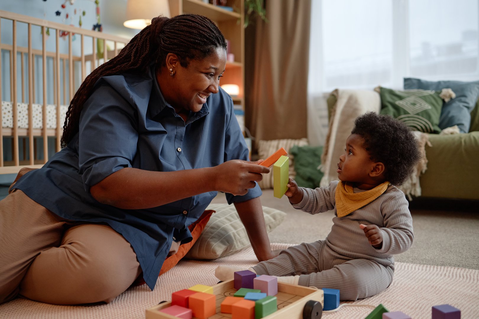 Smiling Black woman looking at little daughter with love and affection spending time with baby girl playing building blocks