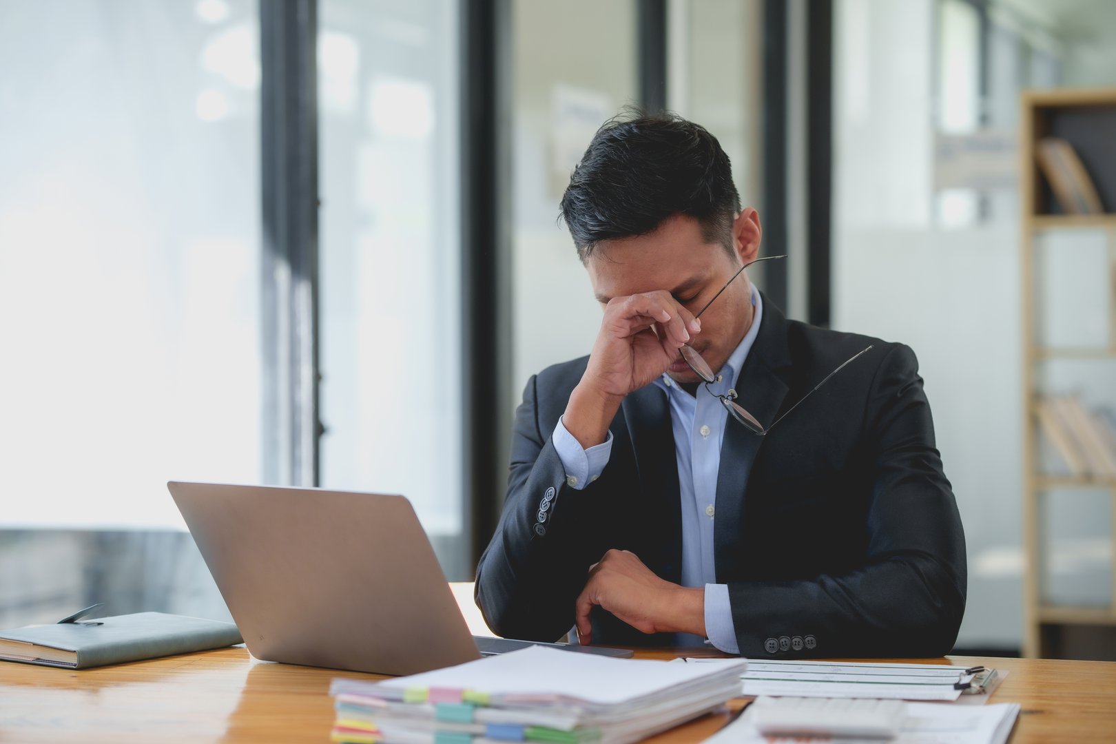 Asian businessman feeling stressed and tired at workplace. Work stress and mental health concept.