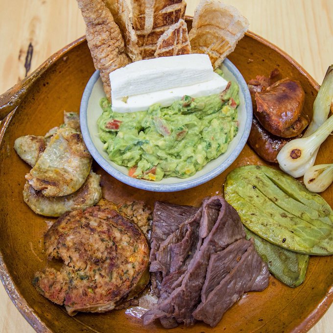 Mexican platter with grilled meats, chicharrón, nopales, spring onions, and guacamole with cheese.