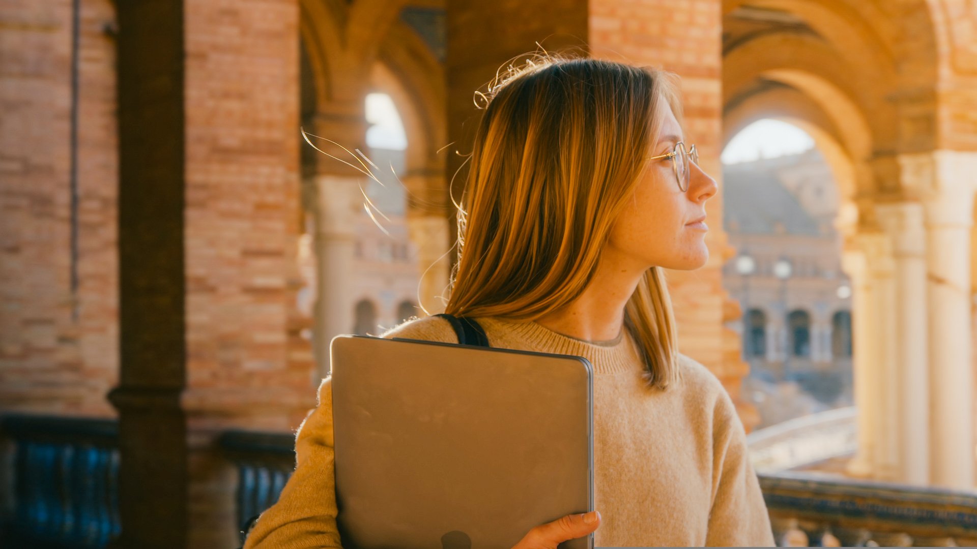 Portrait shot of beautiful young woman walk in sunny corridor of campus building. Female student or professor hold papers and laptop. Education concept. Study abroad. Cinematic real candid portrait
