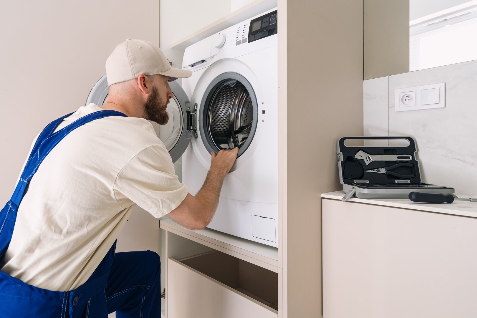 A laundry technician performs maintenance on a sleek, automatic washing machine located in a contemporary bathroom. Concepts of warranty service and yearly checking of household appliances