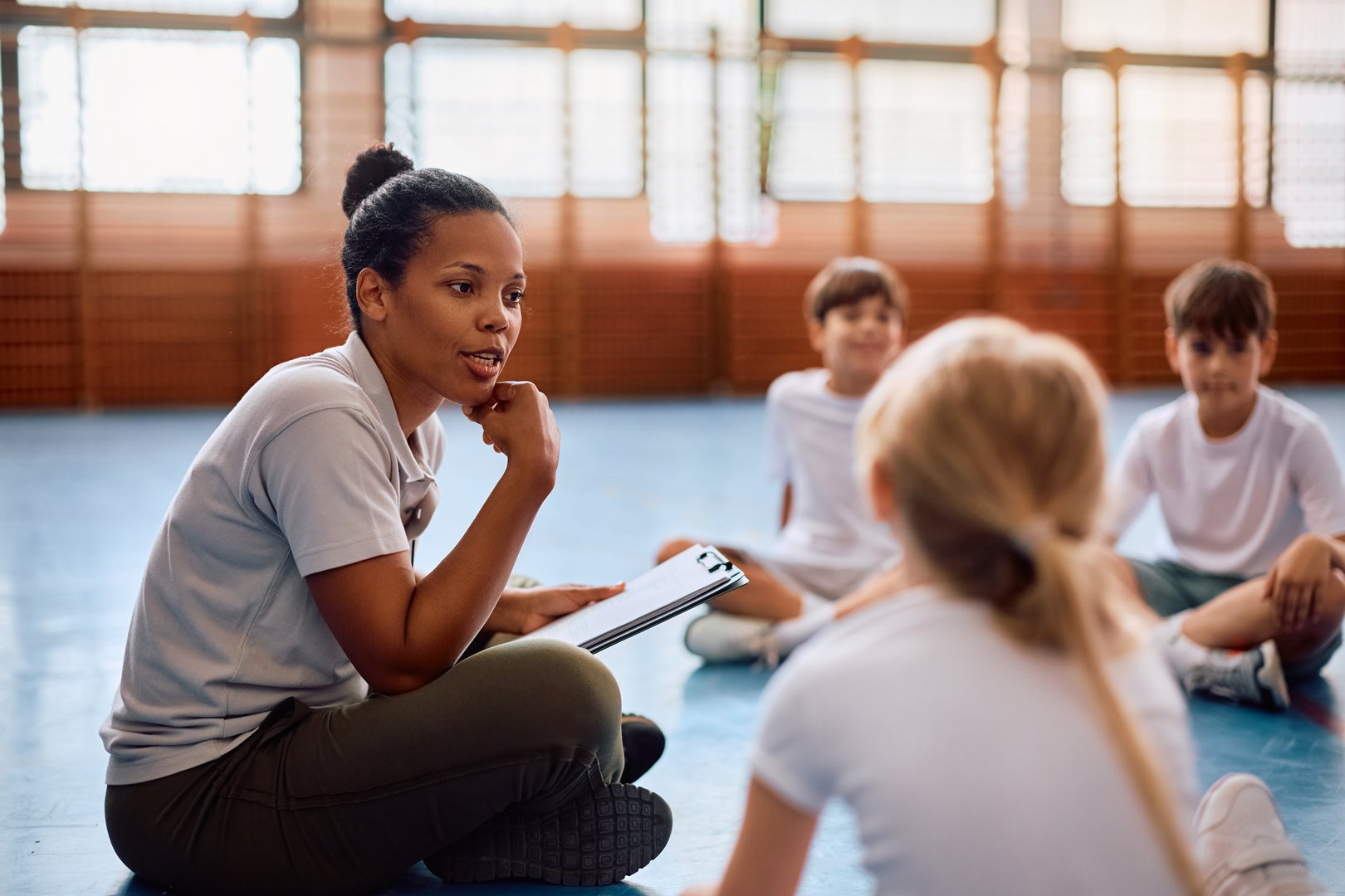 African American physical education teacher communicating with her students at school gym.