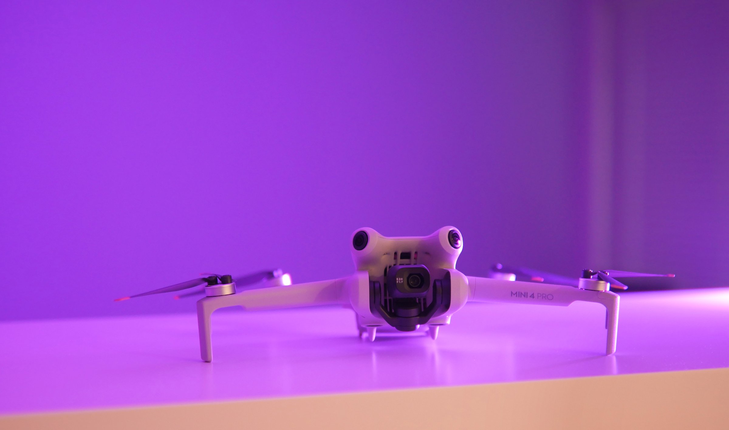 Unfolded DJI Mini 4 Pro drone on display in frontal view  against a purple background.