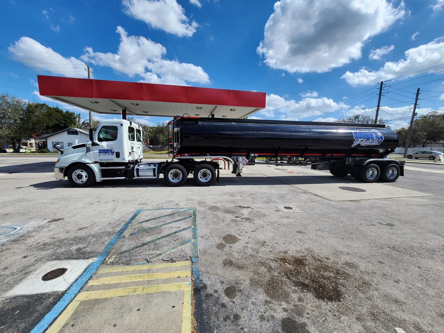 A large tanker truck parked at a gas station under a partly cloudy sky.