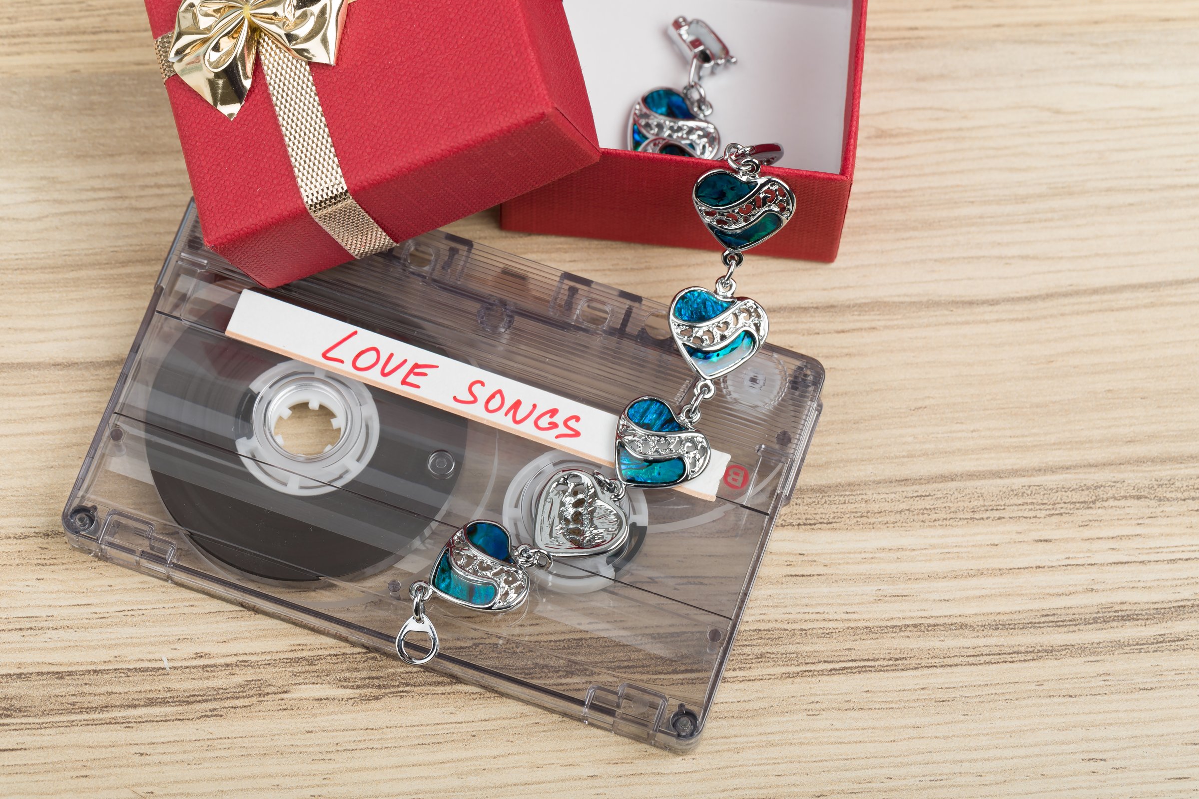 Audio cassette tape with bracelet and present box, label text love songs on wooden backgound. Valentine postcard