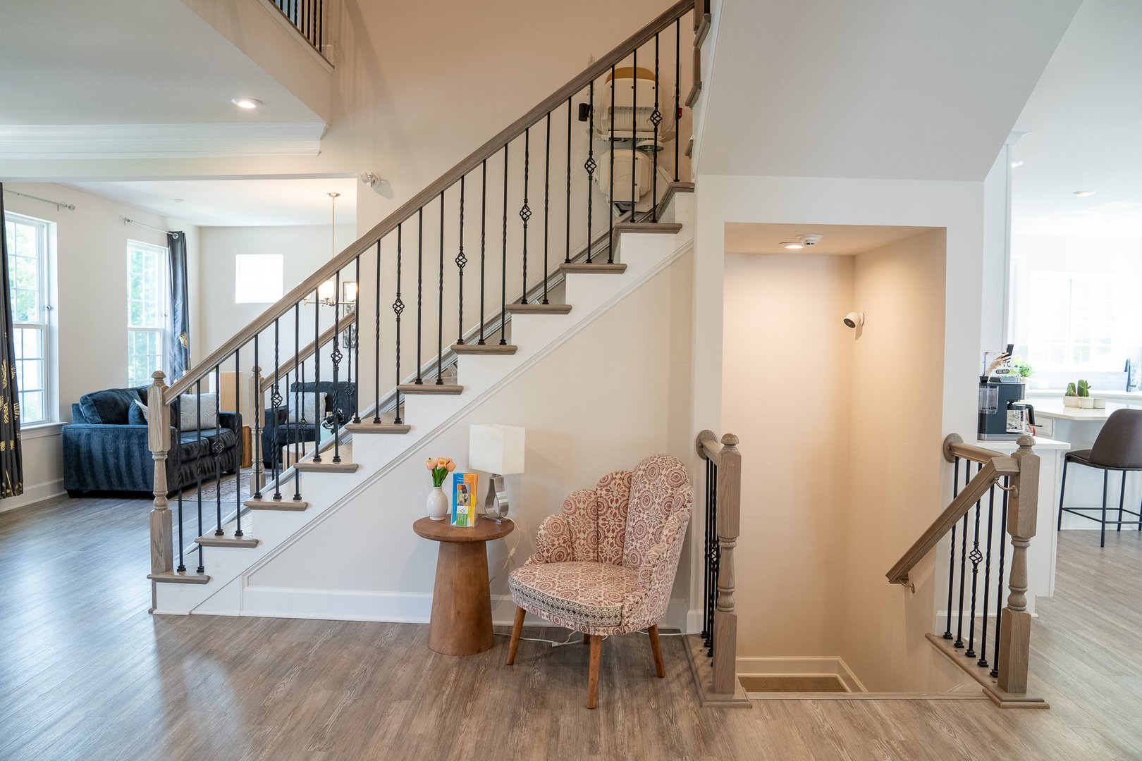 Modern living area with a staircase, armchair, side table, and light hardwood flooring. Bright natural light from windows.