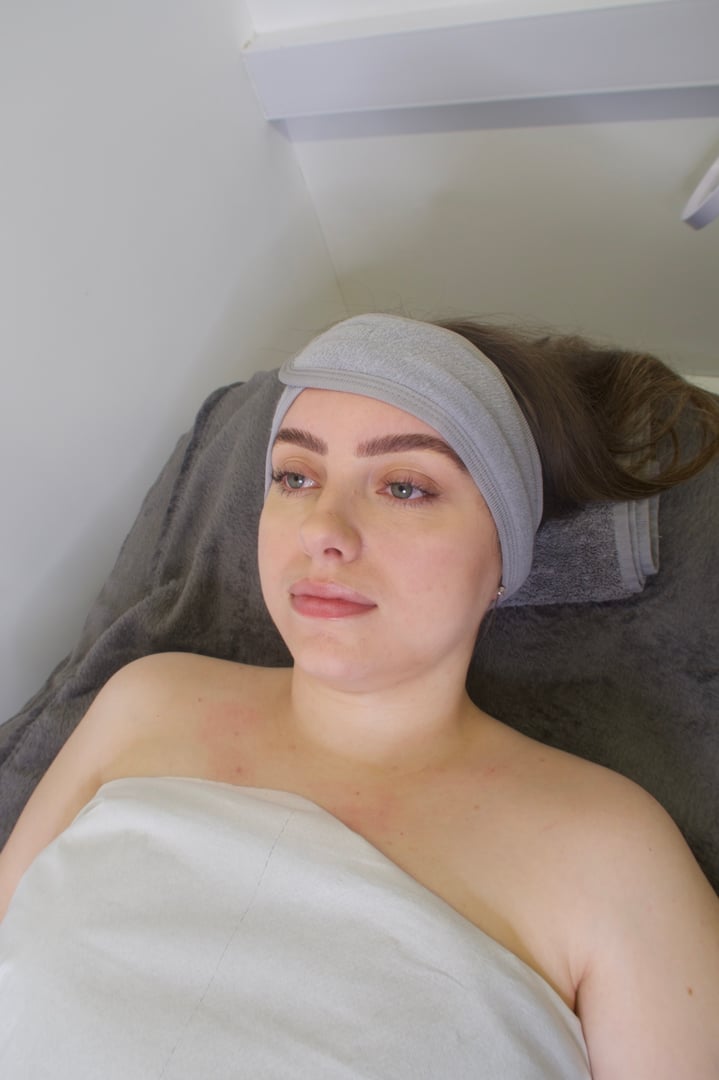 Person lying on a spa bed, wearing a gray headband, wrapped in a towel, with a calm expression.