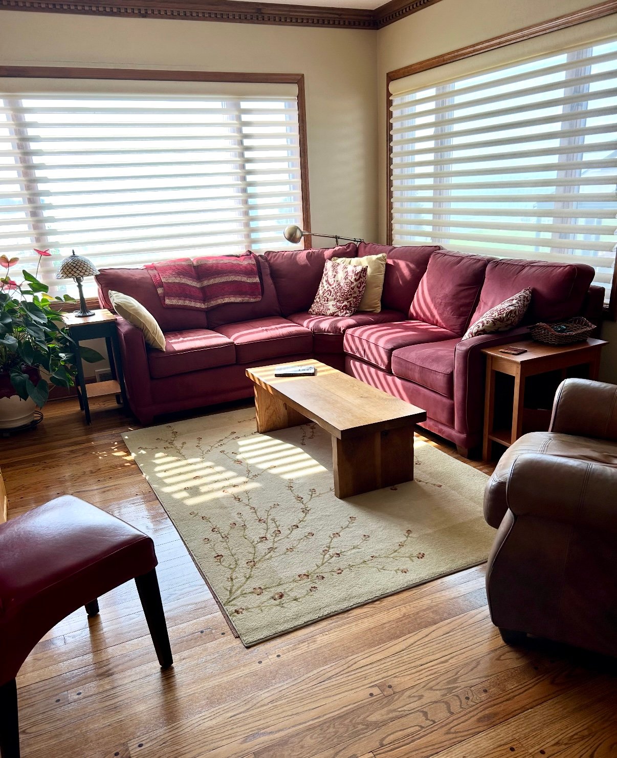A cozy living room with a red sectional sofa, wooden coffee table, patterned rug, and large windows with blinds.