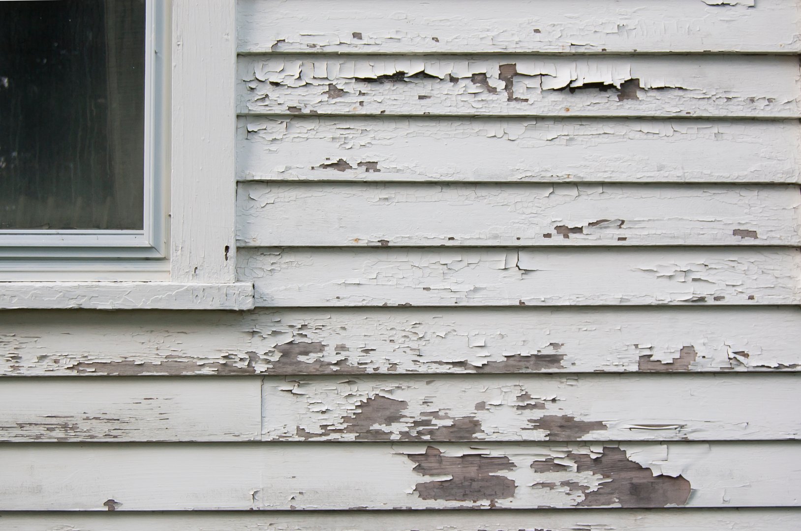 Peeling white paint on a calpboard hose with part of window