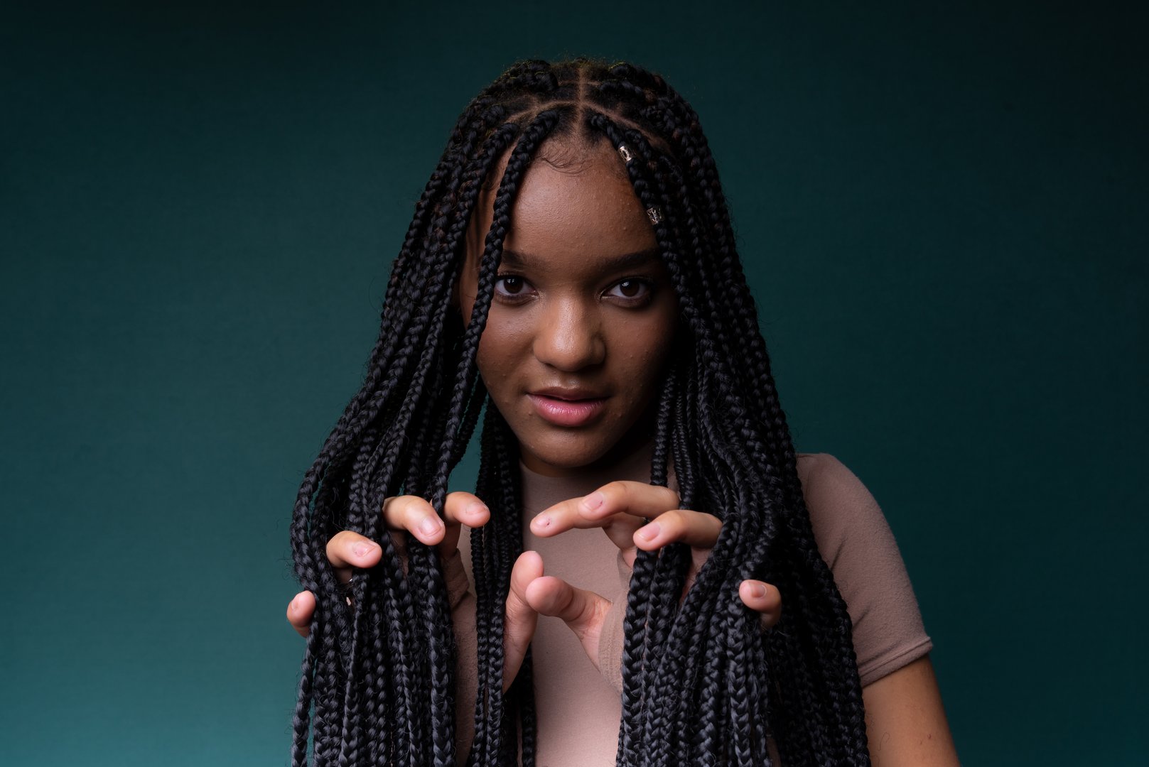 Young pretty black woman showing her hands through her braided hair. Isolated on dark cyan background.