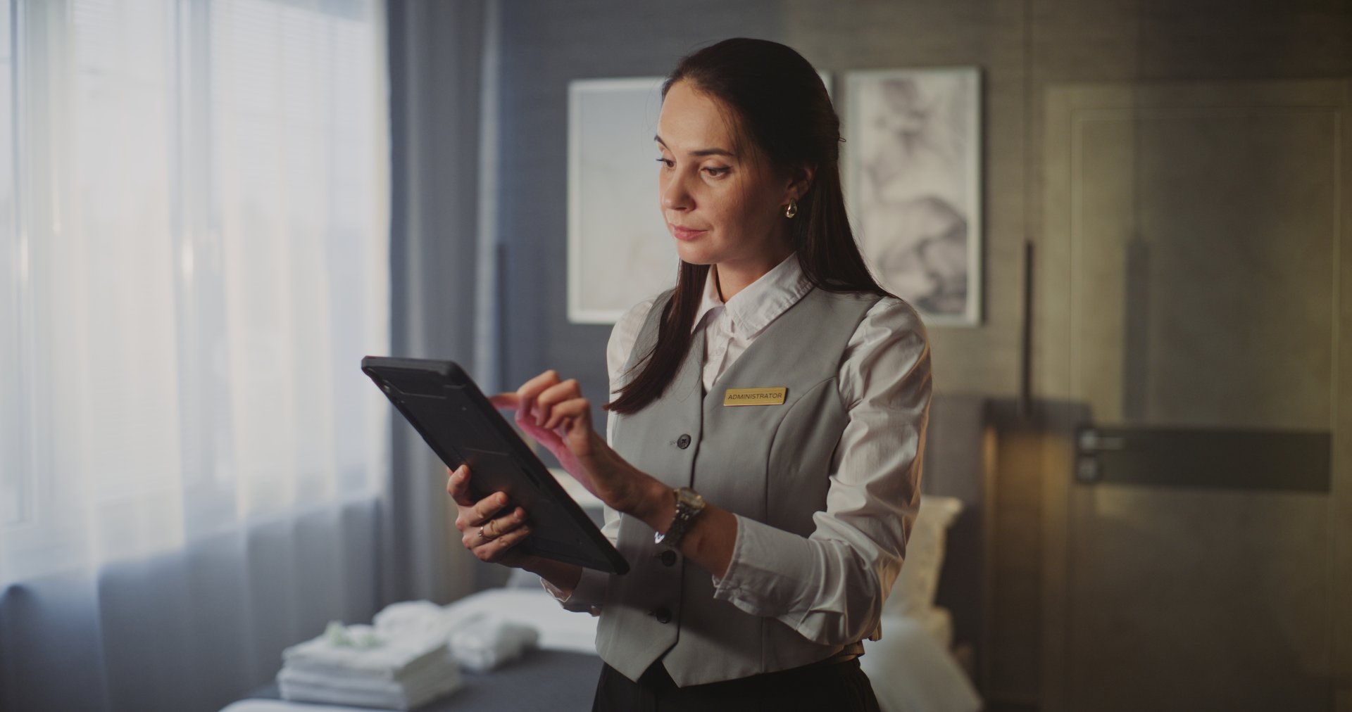 Smiling Young Female Hotel Service Professional in Uniform Holds Tablet, Standing Confidently in Modern Luxury Hotel Room. Concept of Hospitality Management and High End Customer Service. Portrait.
