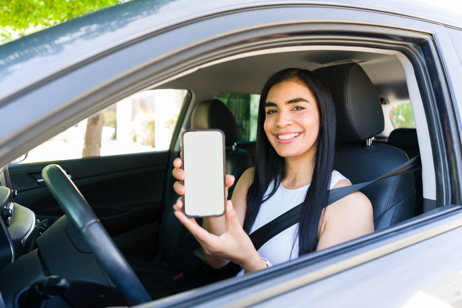 Rideshare driver holding a mobile phone app displaying a blank screen while seated inside a car, ready for passenger bookings