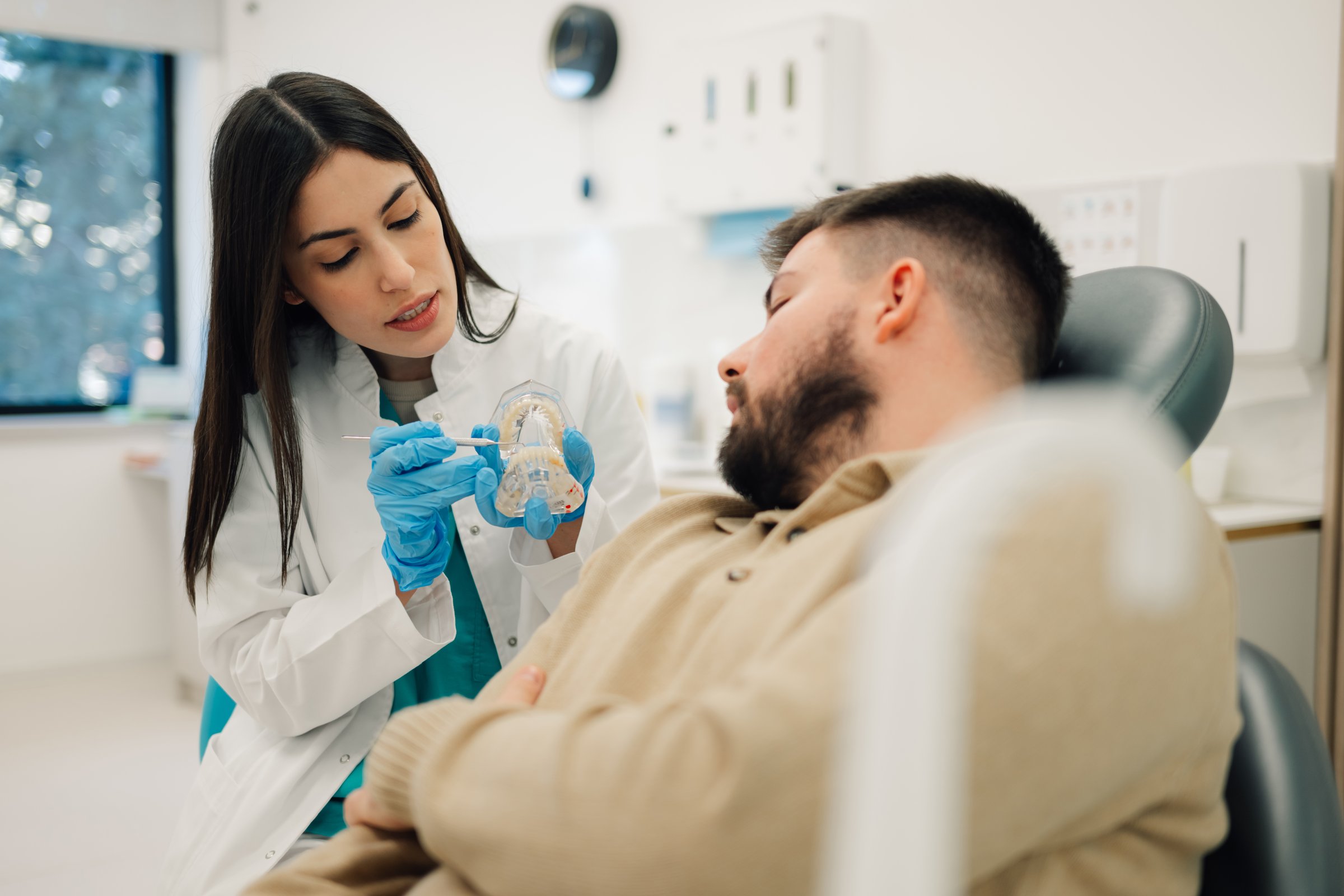 Female dentist explaining dental treatment to a patient using a teeth model
