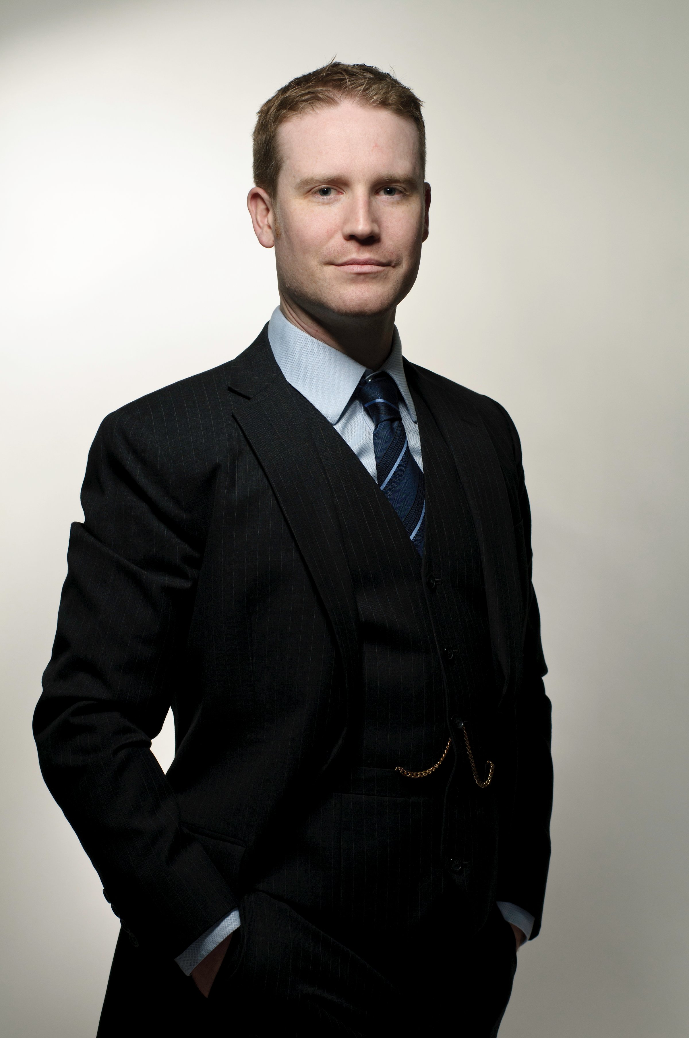 Confident businessman on a grey background.  This photo shows a man in a tailored three piece suit with pocket watch and chain.  This image is of a real man (non model) with no makeup or professional re-touching.