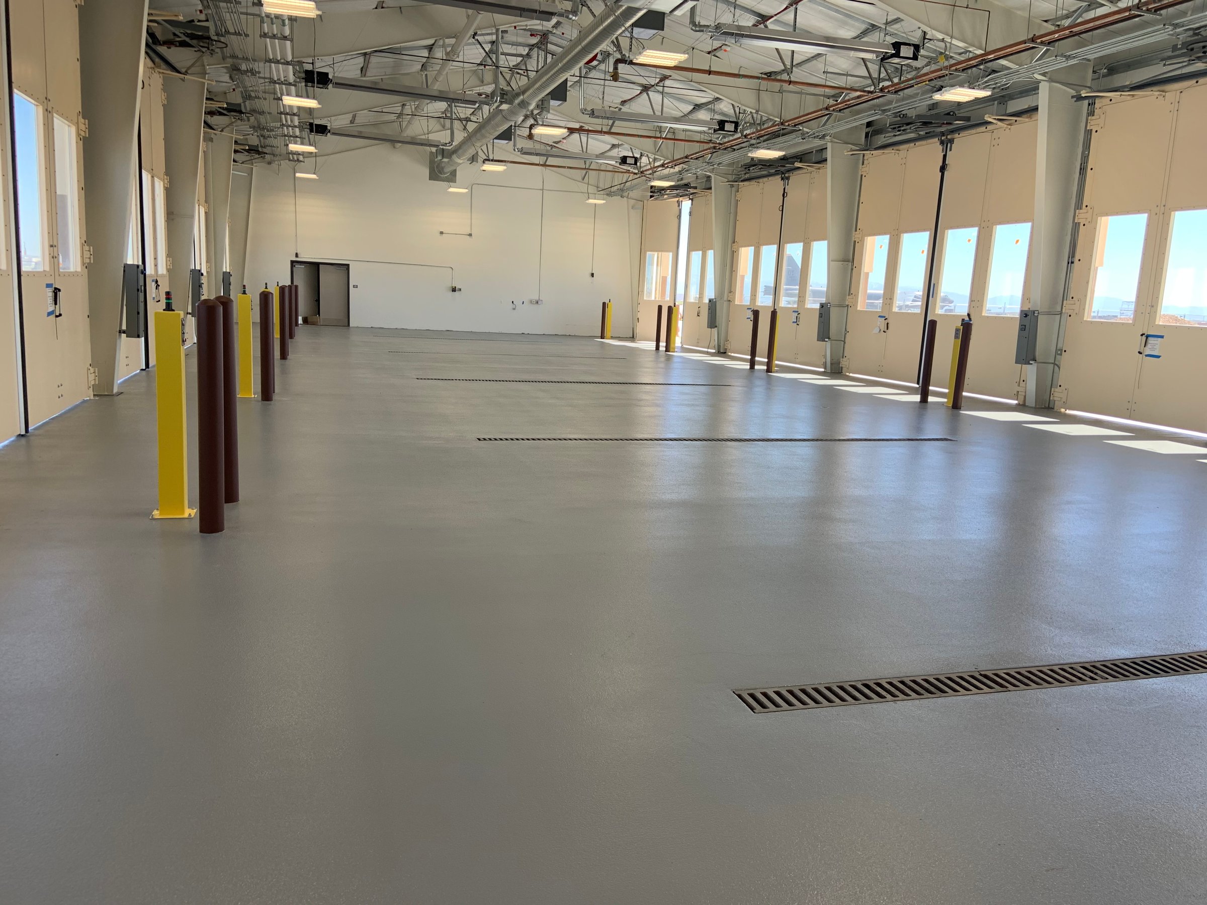 Large, empty warehouse interior with polished concrete floor, high ceiling, and large windows on one side.