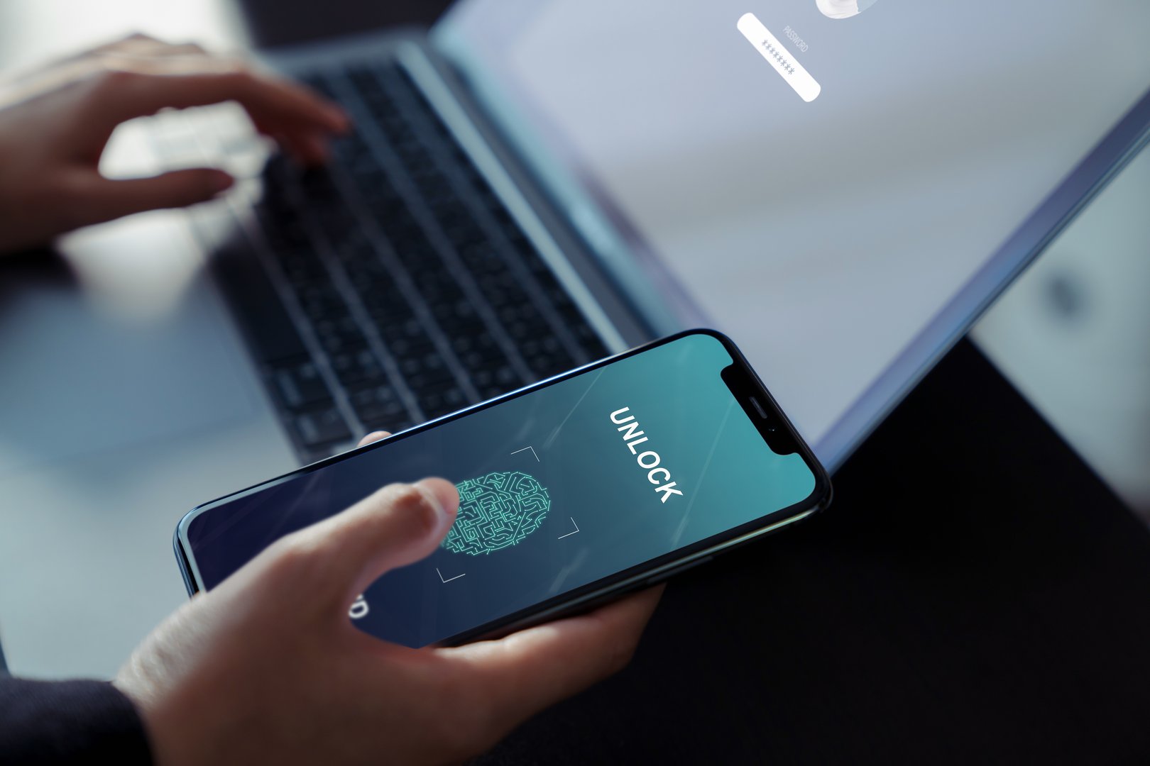 Businessman hand scanning fingerprint on smartphone to unlock mobile phone to laptop computer, Concept security in identity technology. 