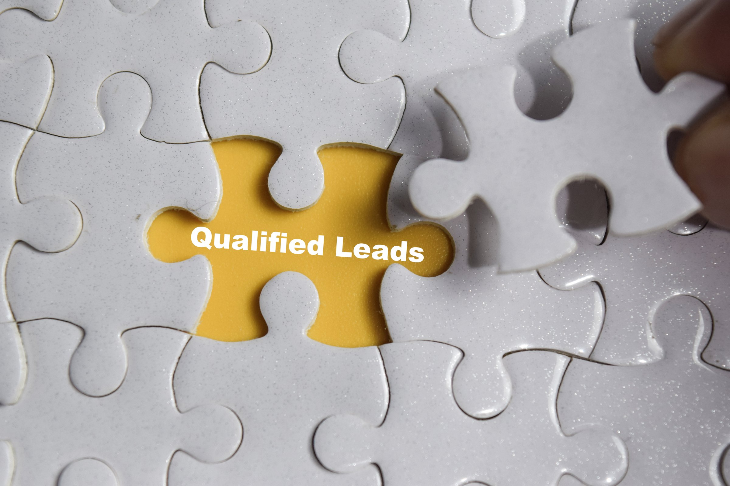 Hand holding piece of jigsaw puzzle with word Qualified leads. Business and finance concept