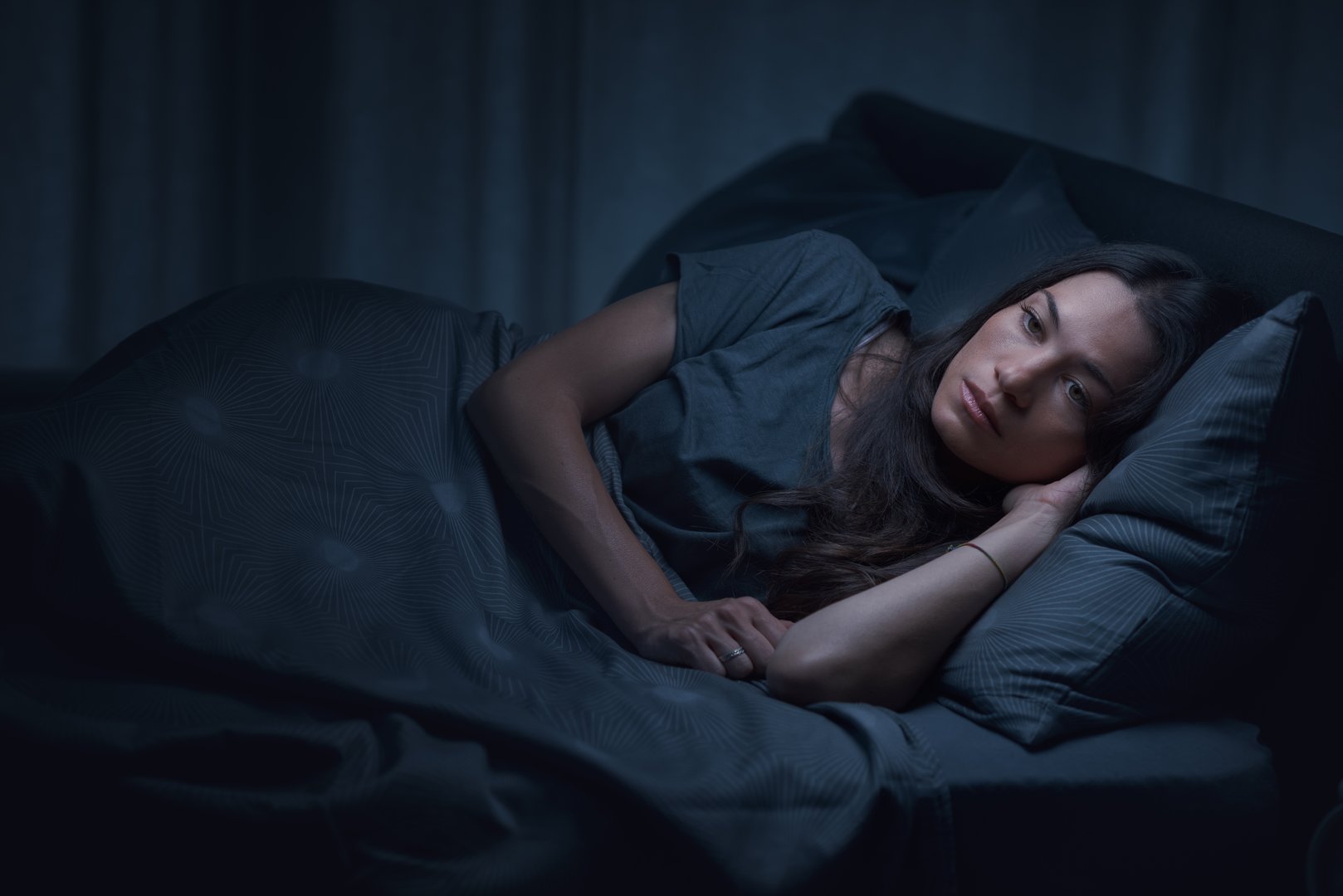 Sad pensive woman lying in bed at night, she is worried and suffering from insomnia