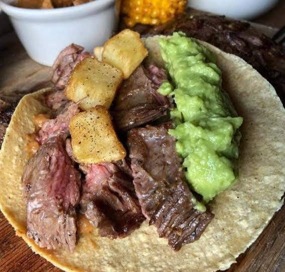 A taco with grilled beef, diced potatoes, and guacamole on a corn tortilla.