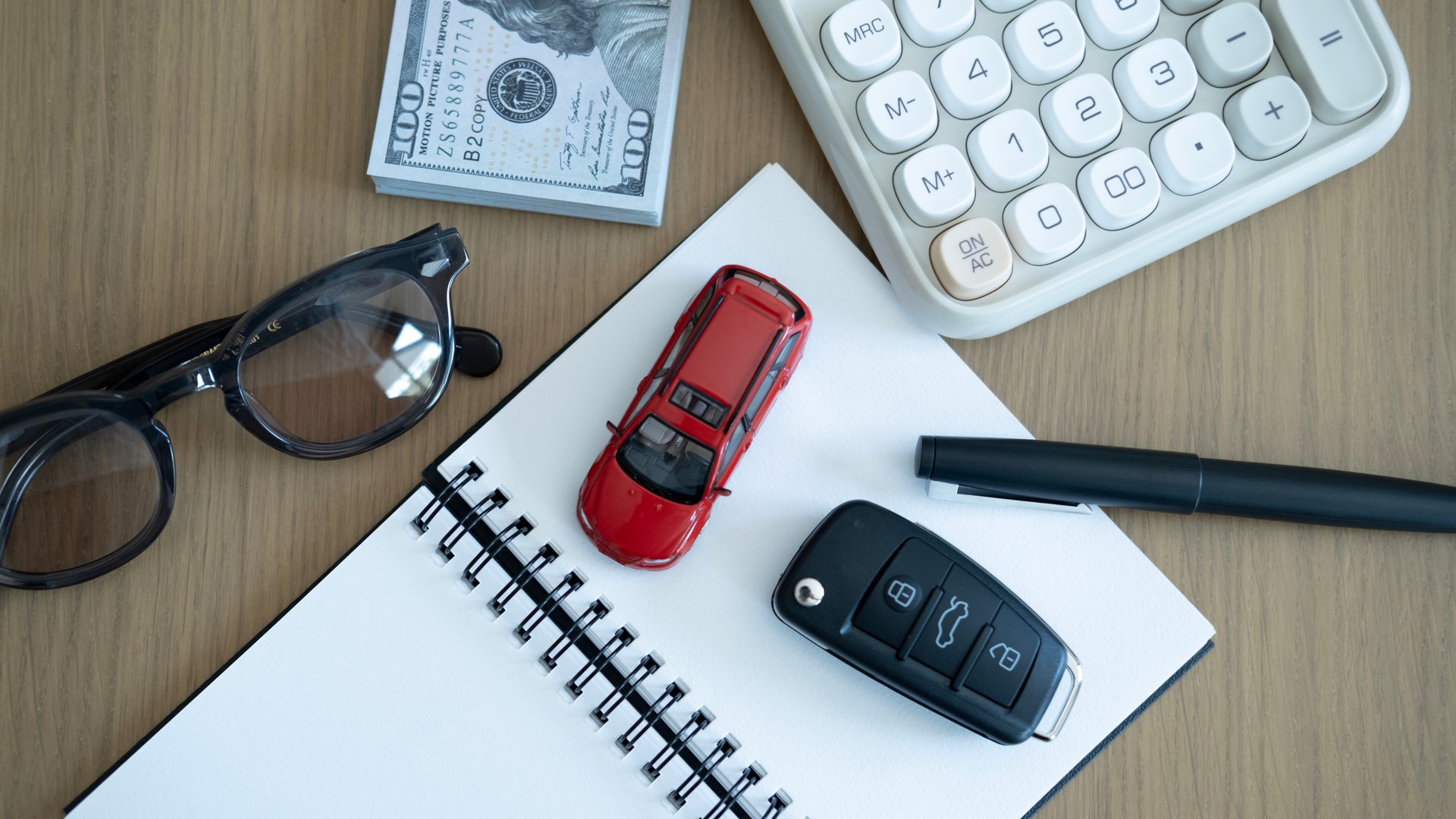 Top view of red toy car on notebook with calculator and money