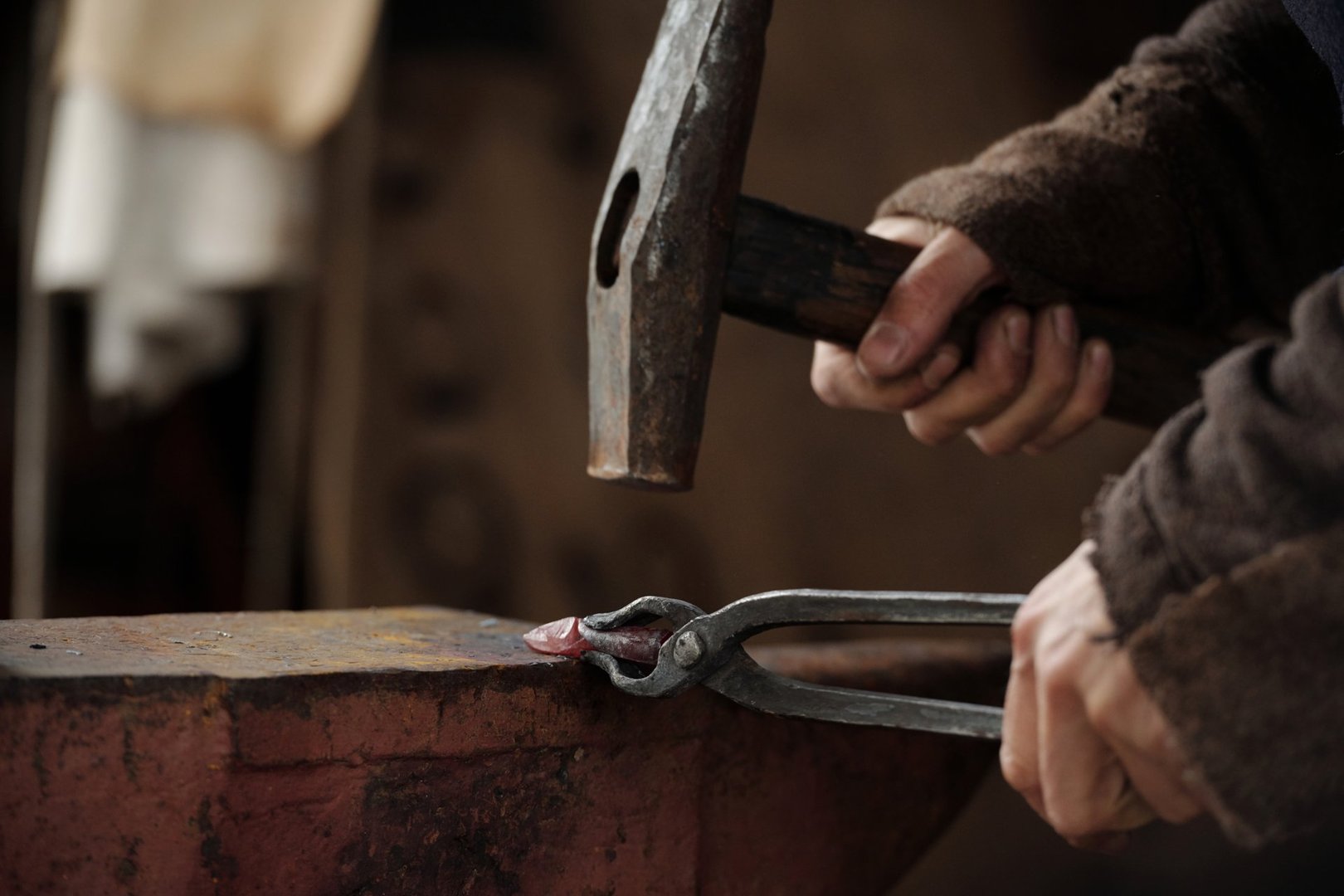 Close-up of hands hammering metal on anvil, showcasing traditional blacksmithing tools and techniques in action, highlighting craftsmanship and attention to detail