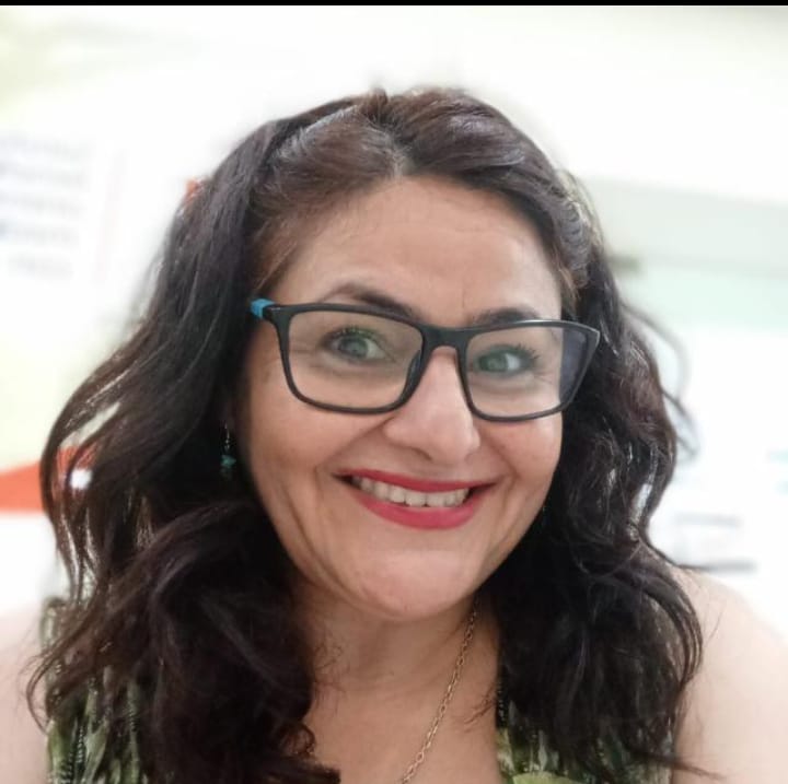 Woman with dark hair and glasses smiling at the camera indoors.