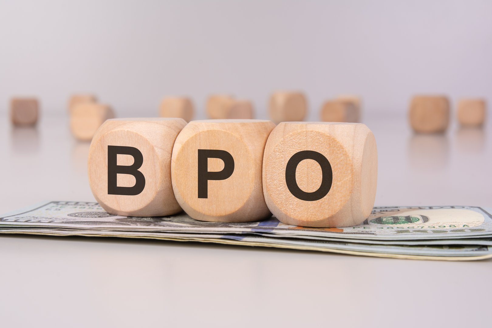 Wooden cubes with 'BPO' letters placed on US dollar bills, symbolizing business process outsourcing, financial management, and corporate efficiency.