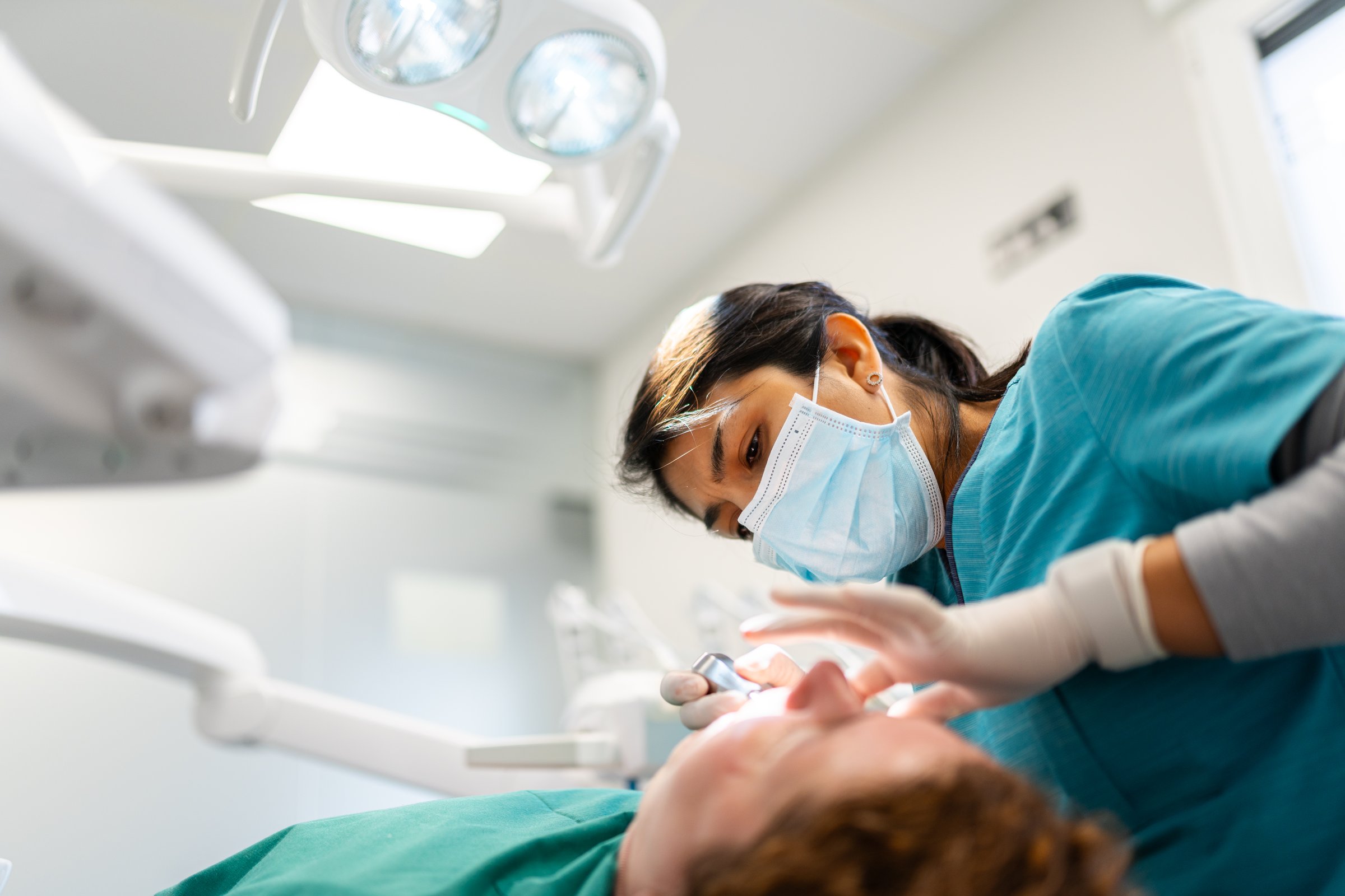 Female dentist in mask and gloves examines patient's teeth during routine dental checkup in a modern, bright clinic setting