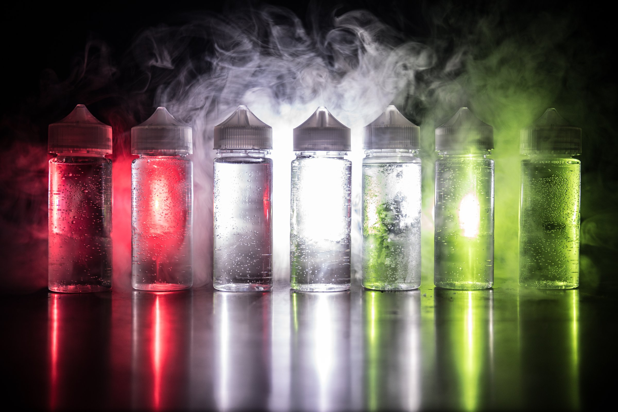Vape concept. Smoke clouds and vape liquid bottles on dark background. Light effects. Selective focus