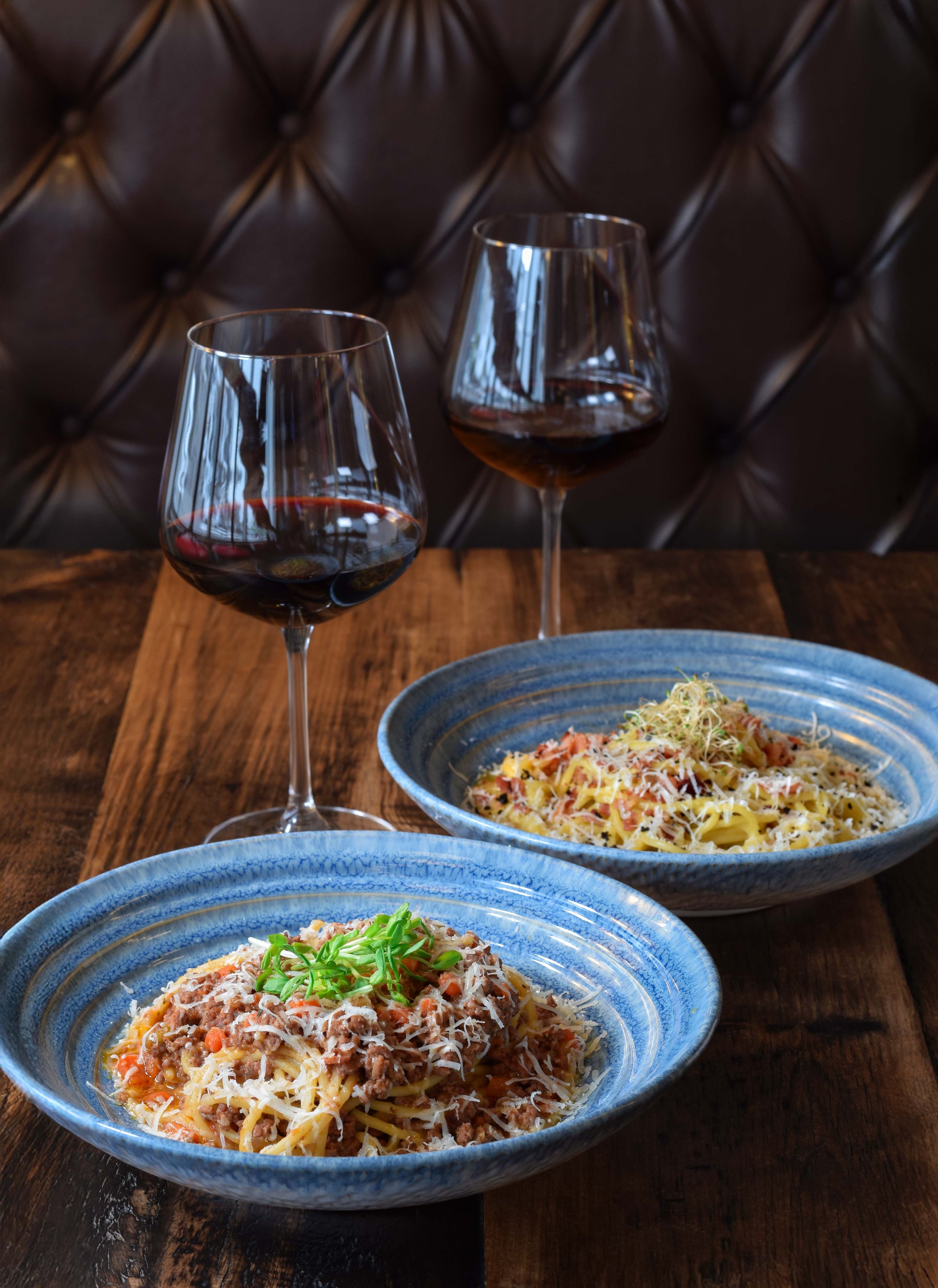 Two bowls of pasta and two glasses of red wine on wooden table