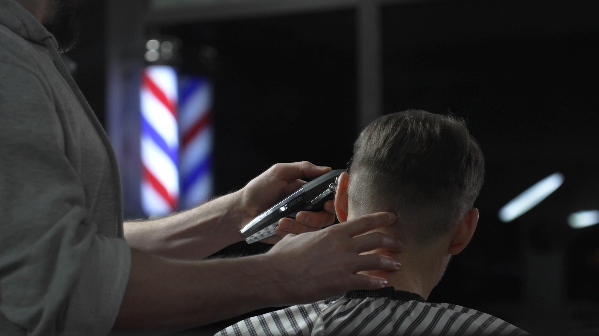 Professional barber skillfully cutting hair of male customer with an electric razor in a modern barbershop, crafting a stylish and contemporary haircut that enhances personal style