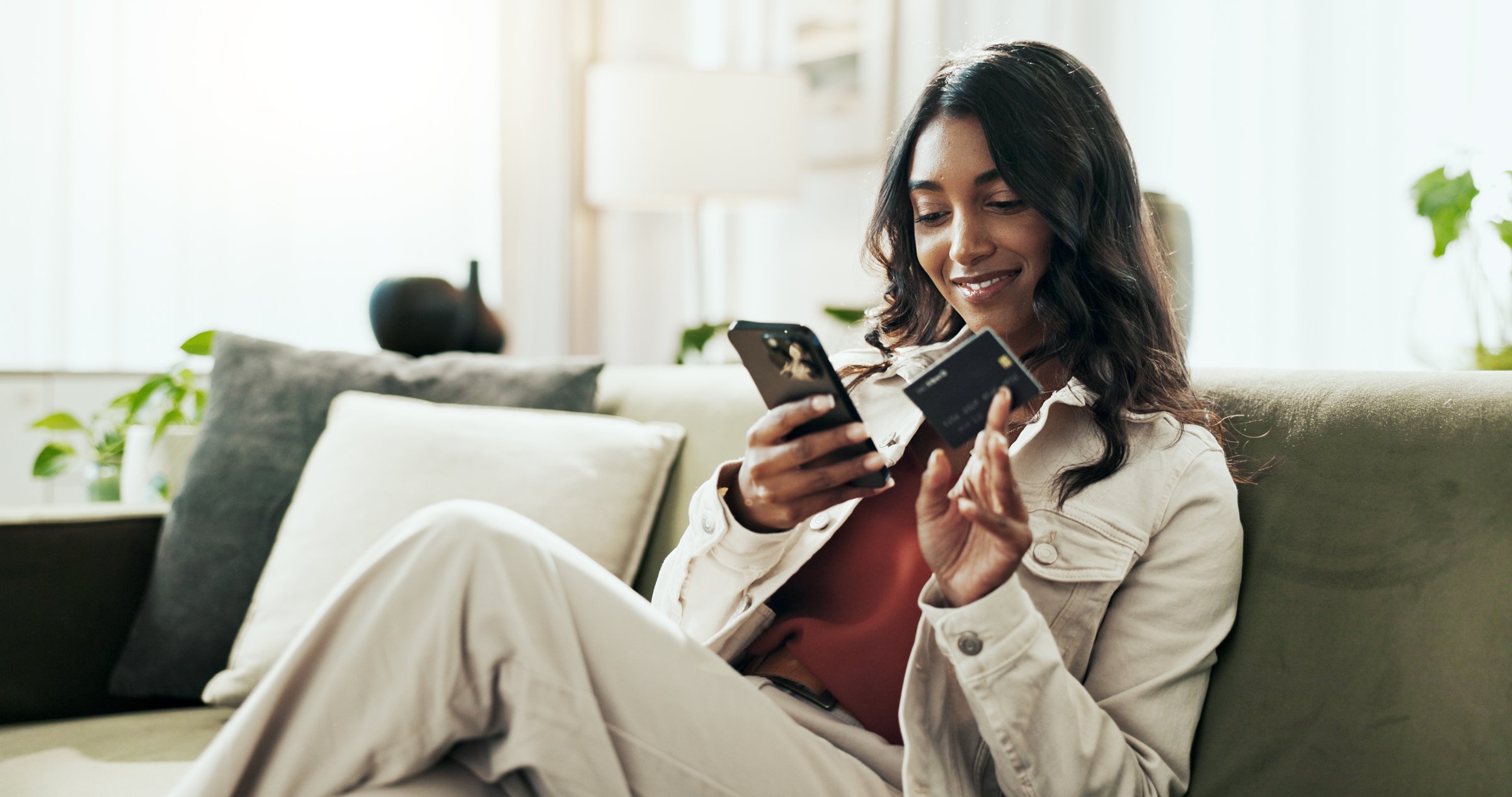 Budget, payment and woman with smartphone, credit card and celebration with savings, investment and smile. House, person and girl on sofa, cellphone and transactions with ecommerce, app and economy