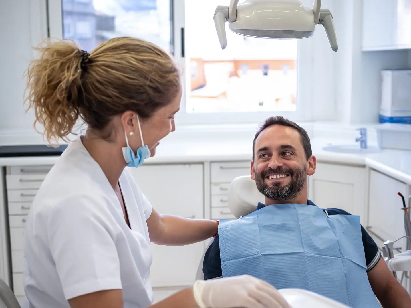 A cheerful patient in a dental chair smiles at a dentist during the appointment. The bright clinic features modern equipment.