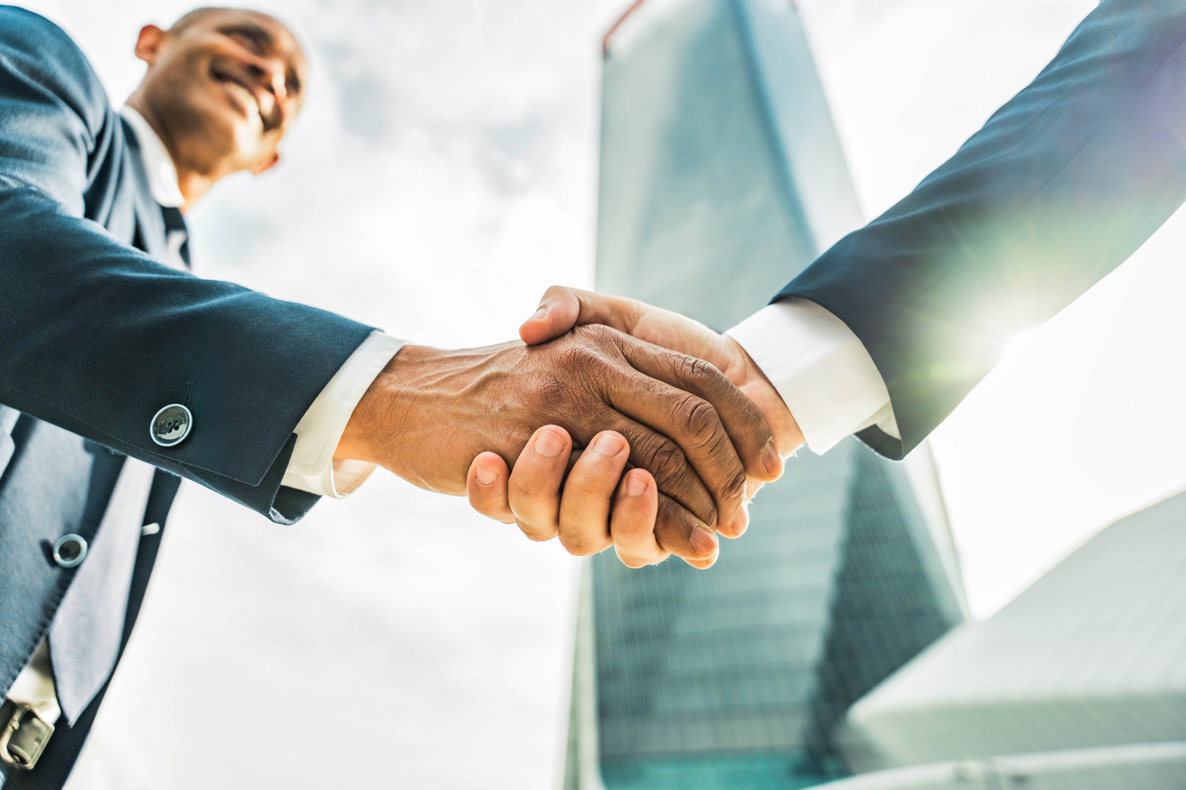 Two business men shaking hands in front of office building outdoors - Concept about leadership, agreement, teamwork and business