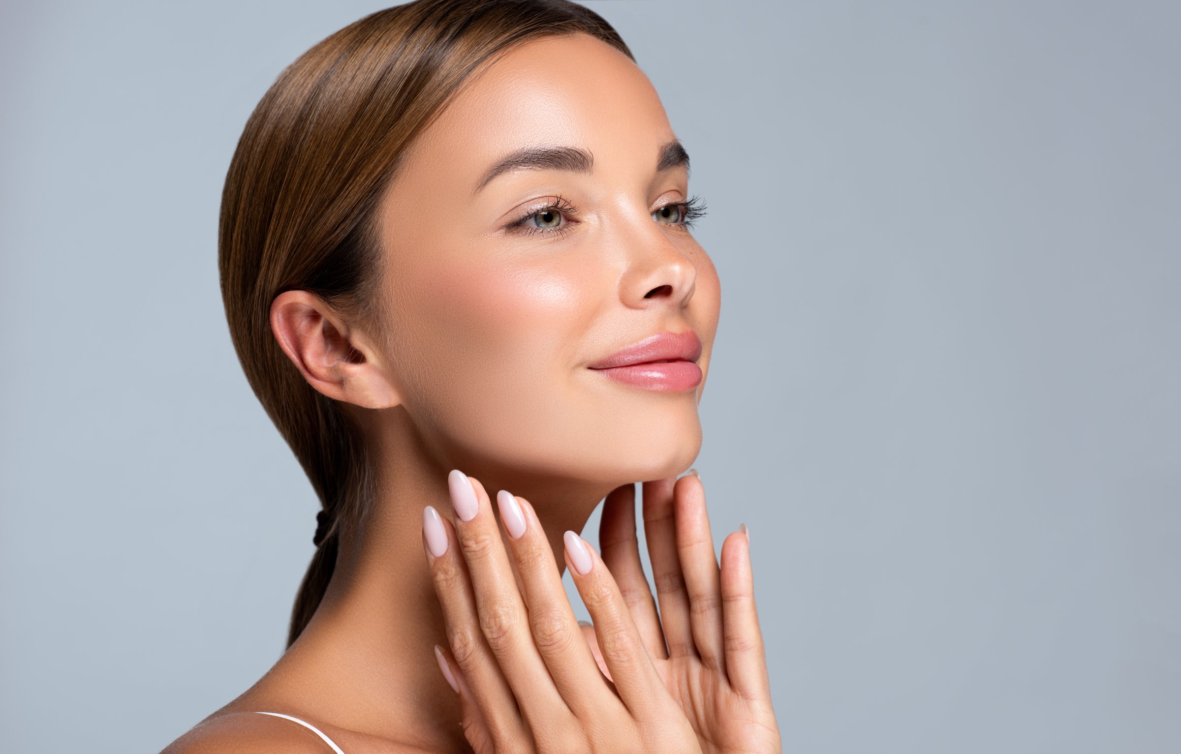 Gorgeous, young, brown haired woman with clean fresh skin is touching the face.  Light smile on the perfect face. Facial treatment, cosmetology, beauty technologies and manicure.