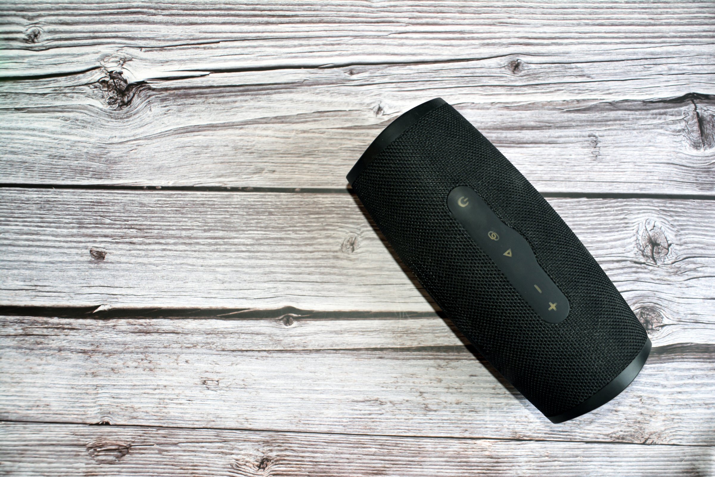 Black wireless speaker on wooden table. Bluetooth speaker. Black speaker on a white wooden background