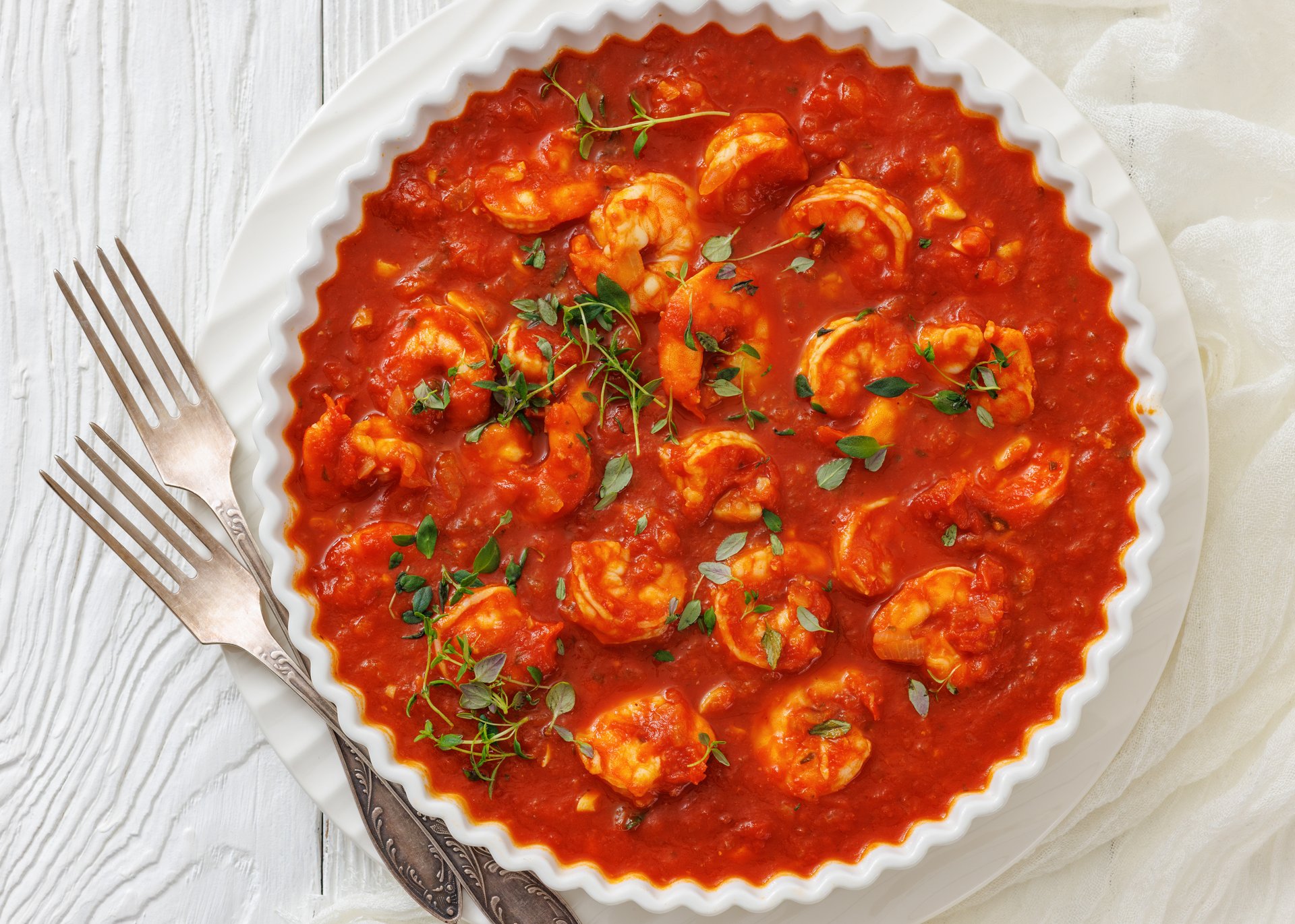 Portuguese Shrimp Mozambique, Shrimp in hot tomato sauce with garlic, onion in white dish on white wood table with forks, horizontal view from above, flat lay, close-up, not AI generated
