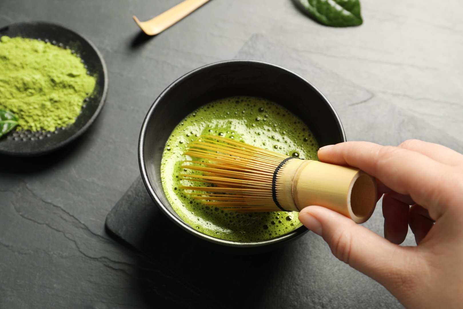 Woman preparing matcha tea at black table, above view
