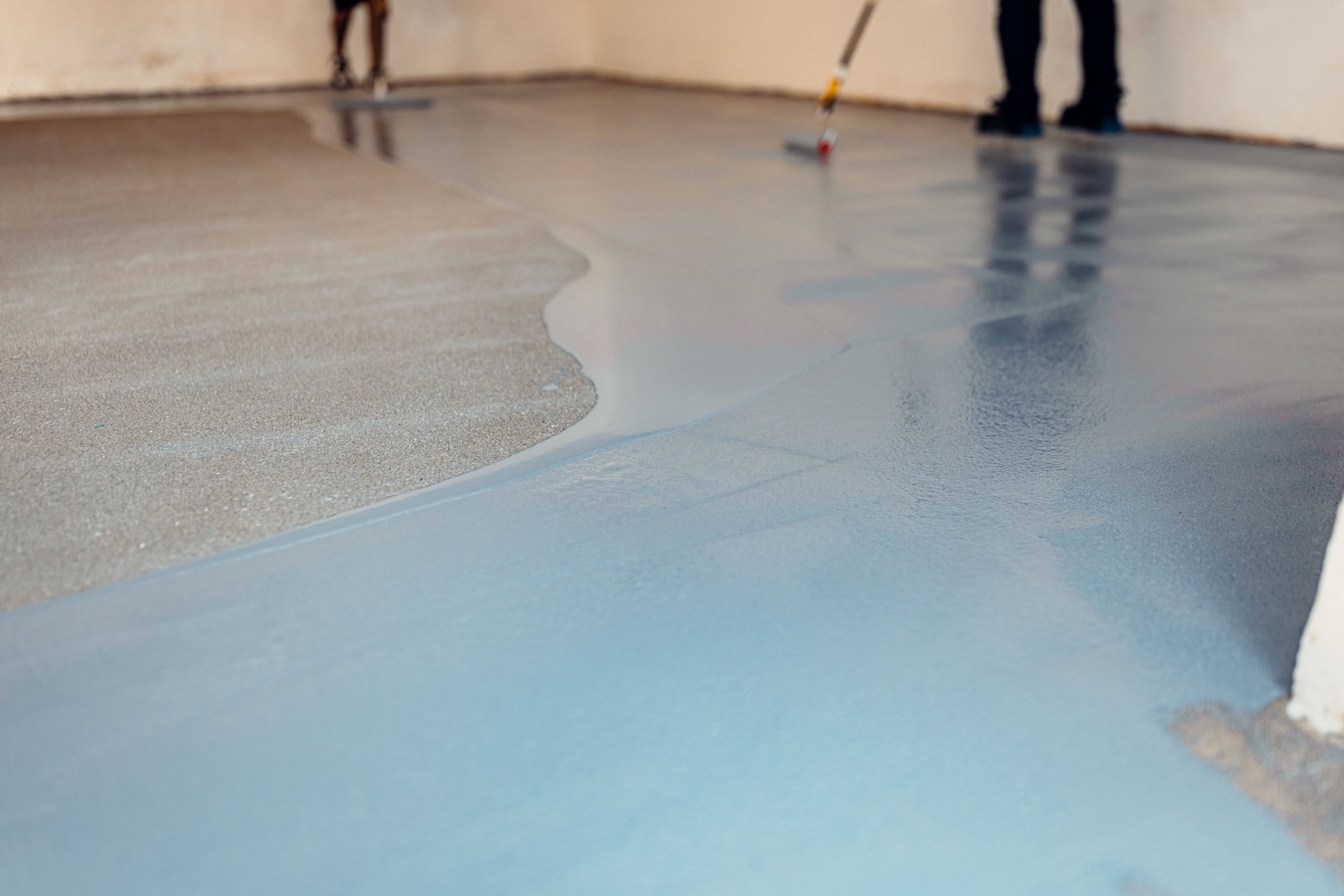 A construction worker apply grey epoxy resin in an industrial hall