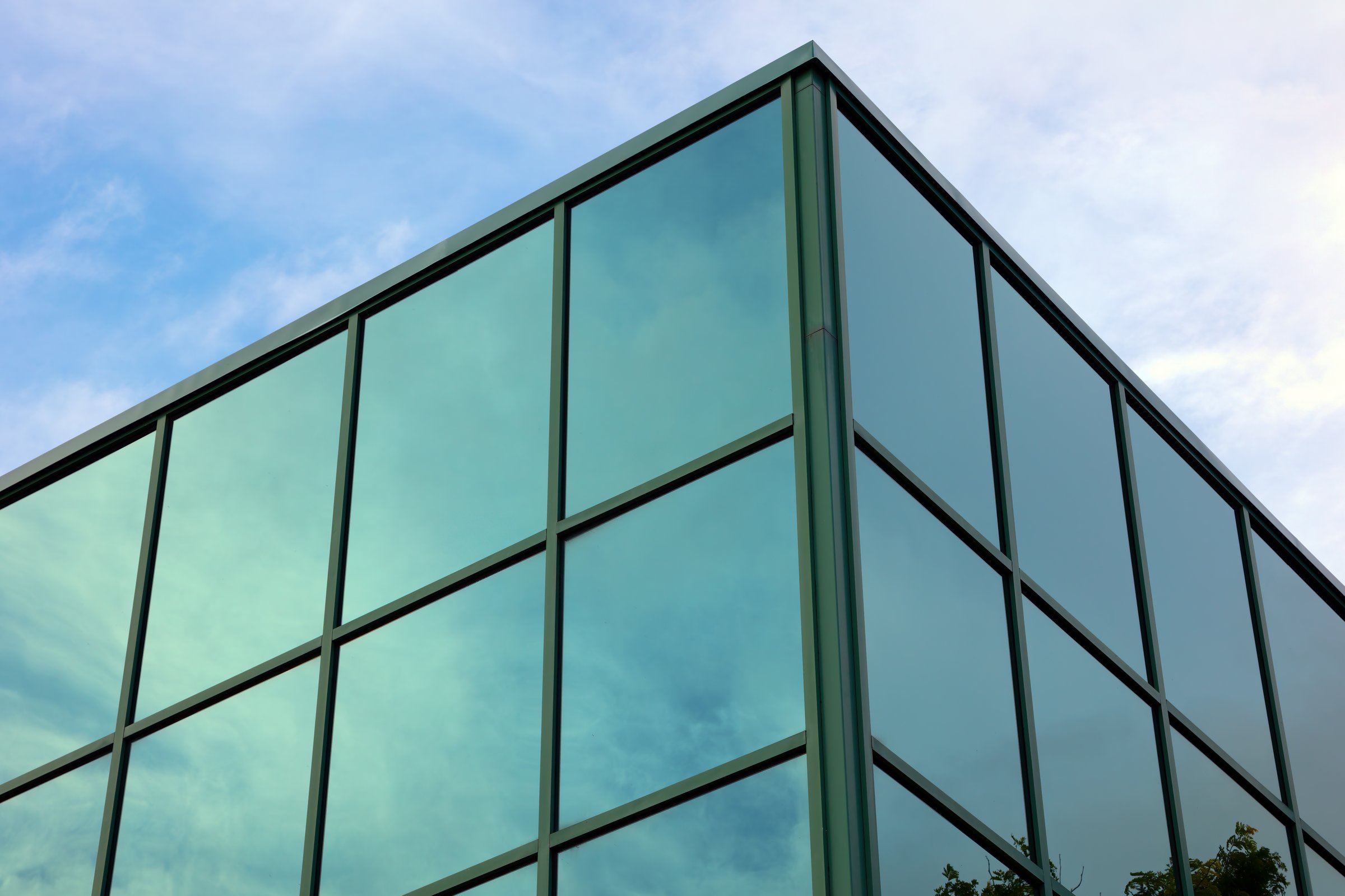 Futuristic glass corner office building with green reflective windows. Capturing urban architecture, geometric design, and morning light in a downtown business district.