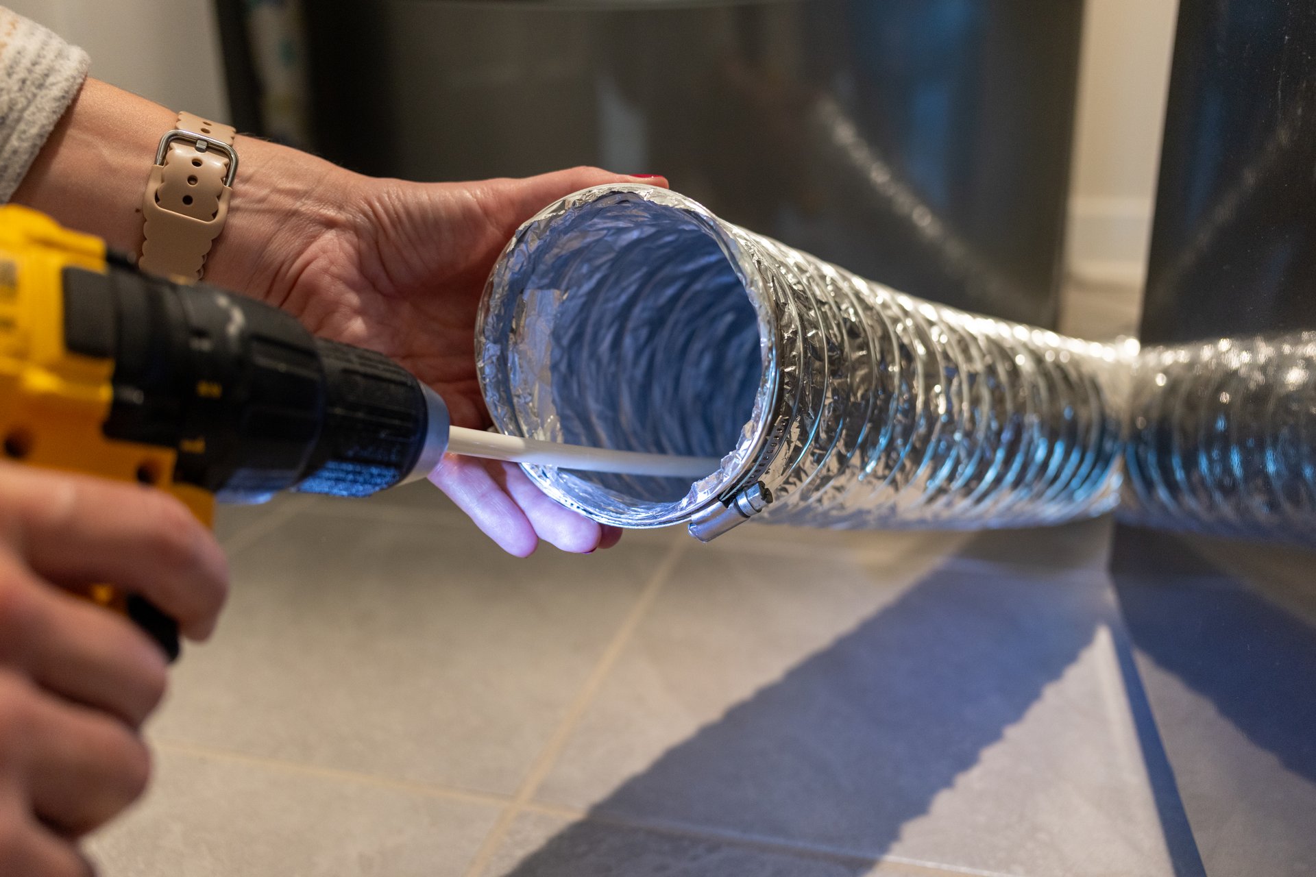 Woman homeowner directs cleaning brush attachment on drill into dryer vent hose